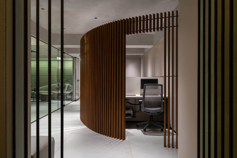 Modern office with curved wooden slat screen divider and ergonomic chair at workstation.