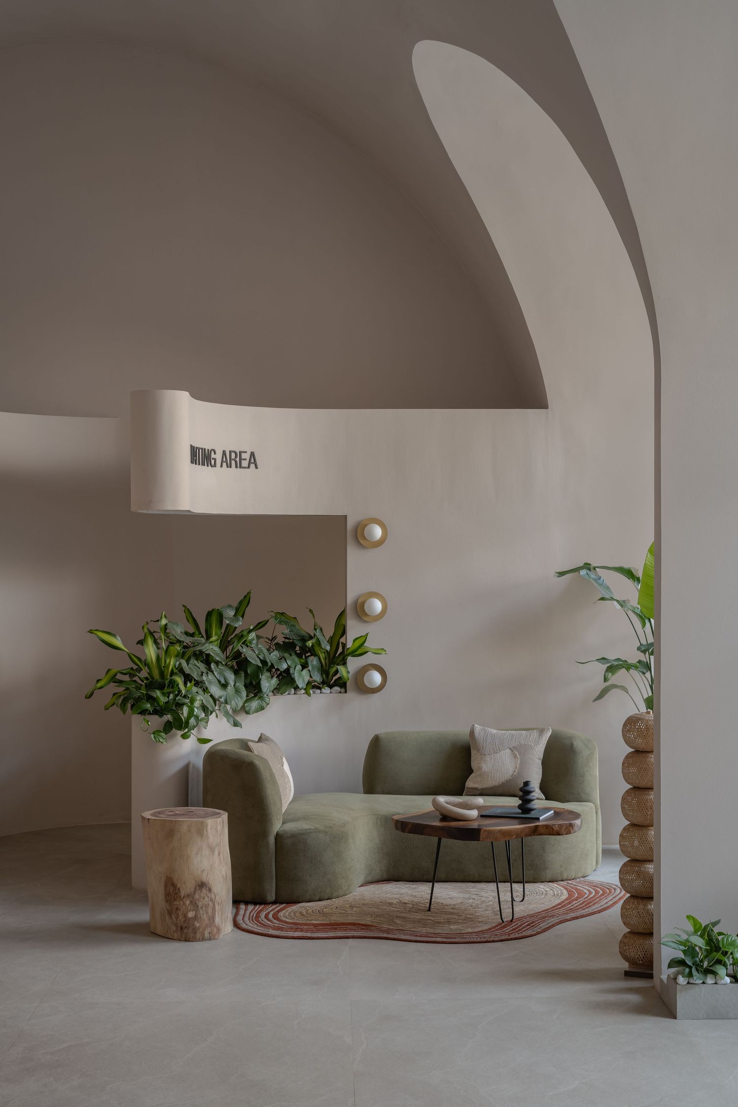 Minimalist waiting area with vaulted ceiling, sage green curved sofa, tropical plants, and decorative spherical column.