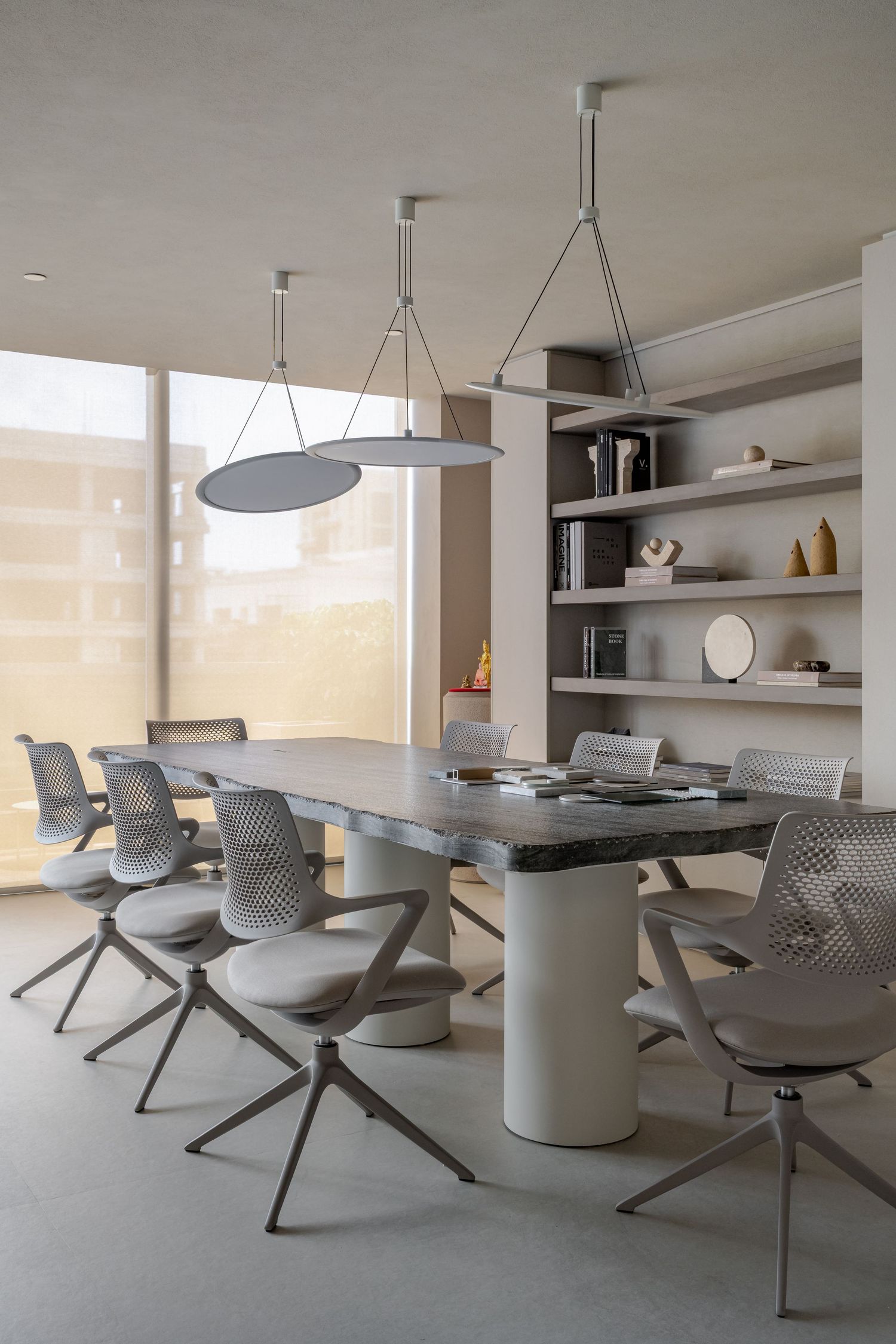 Modern minimalist conference room with gray chairs, large table, pendant lights, and built-in shelving unit near floor-to-ceiling windows.