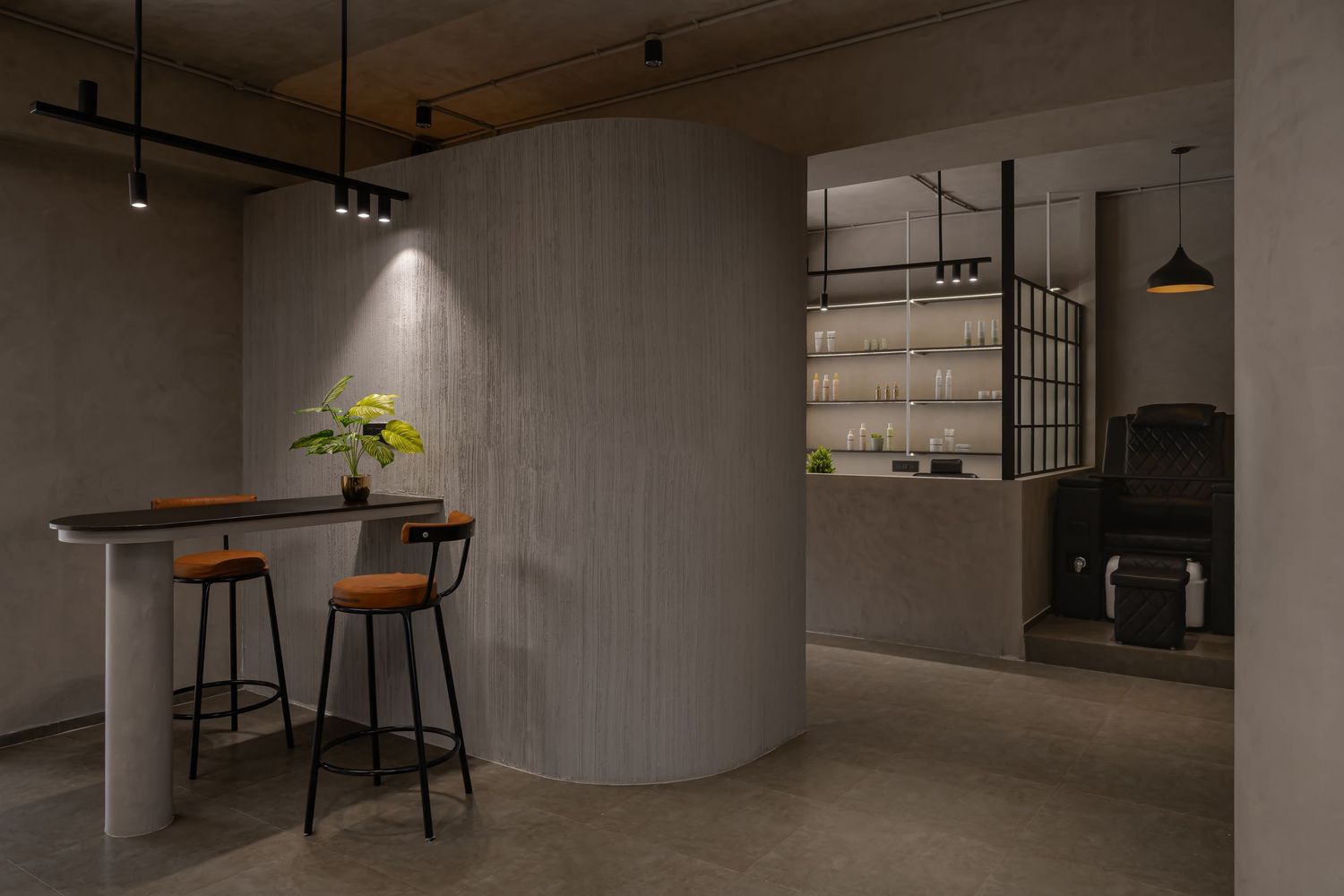 Minimalist salon interior featuring a wooden bar counter with leather stools, curved walls, and backlit product shelving display.