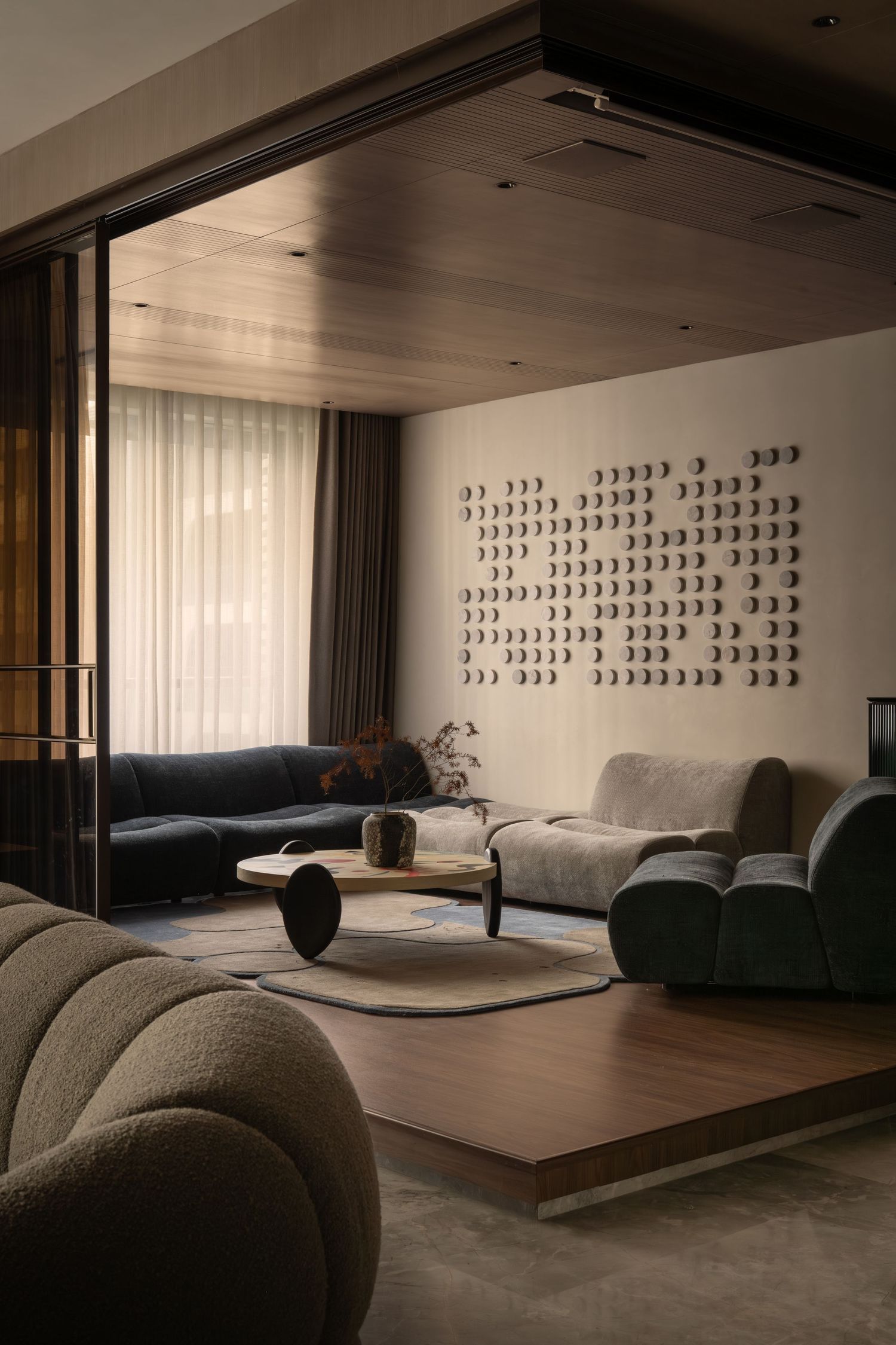 Contemporary lounge with mixed curved sofas, round wood coffee table, and decorative circular wall installation.