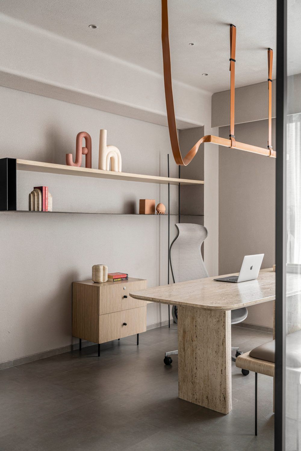 Elegant home office with travertine desk, leather strap pendant light, and decorative wall shelves.