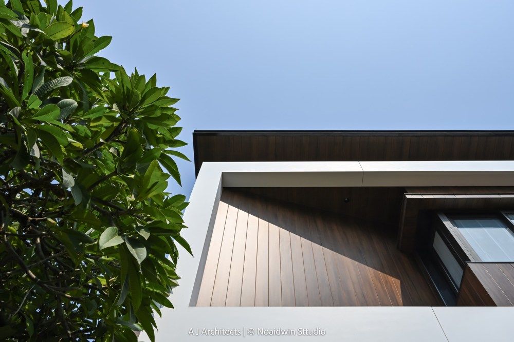 Close-up architectural detail of wood-clad exterior wall with white concrete overhang against blue sky.