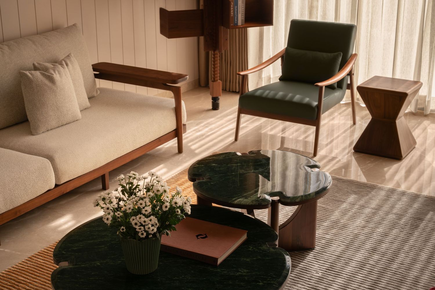 Sophisticated sitting area with cream sofa, green leather chair, dark green marble coffee table, and warm sunlight.