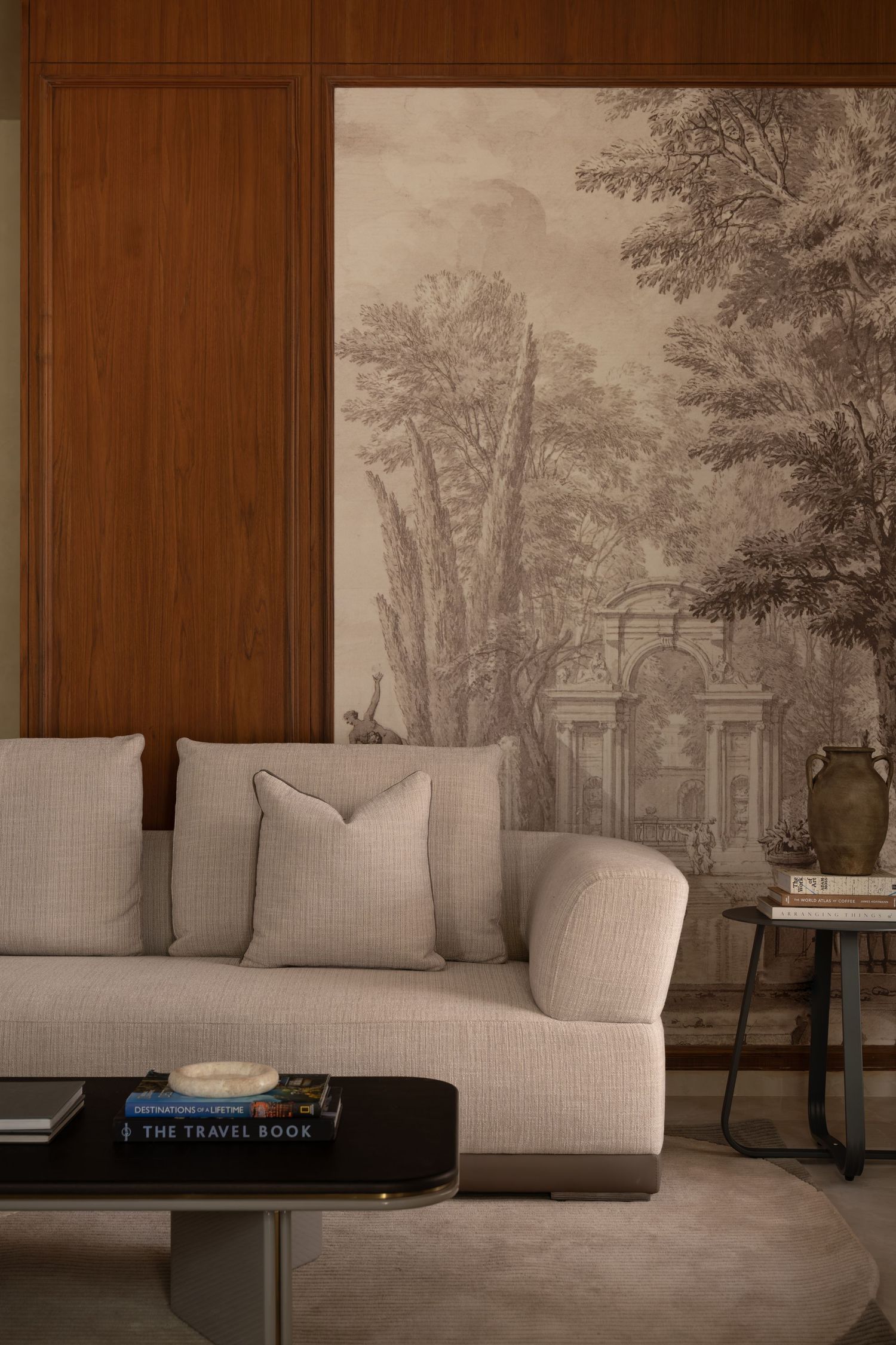 Sophisticated living room featuring a scenic mural wallpaper, beige sofa, and dark coffee table.