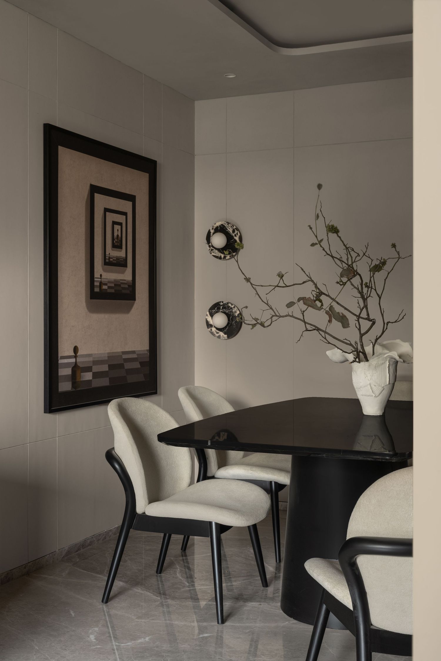 Modern dining room with black round table, cream upholstered chairs, wall art, and decorative branch arrangement.