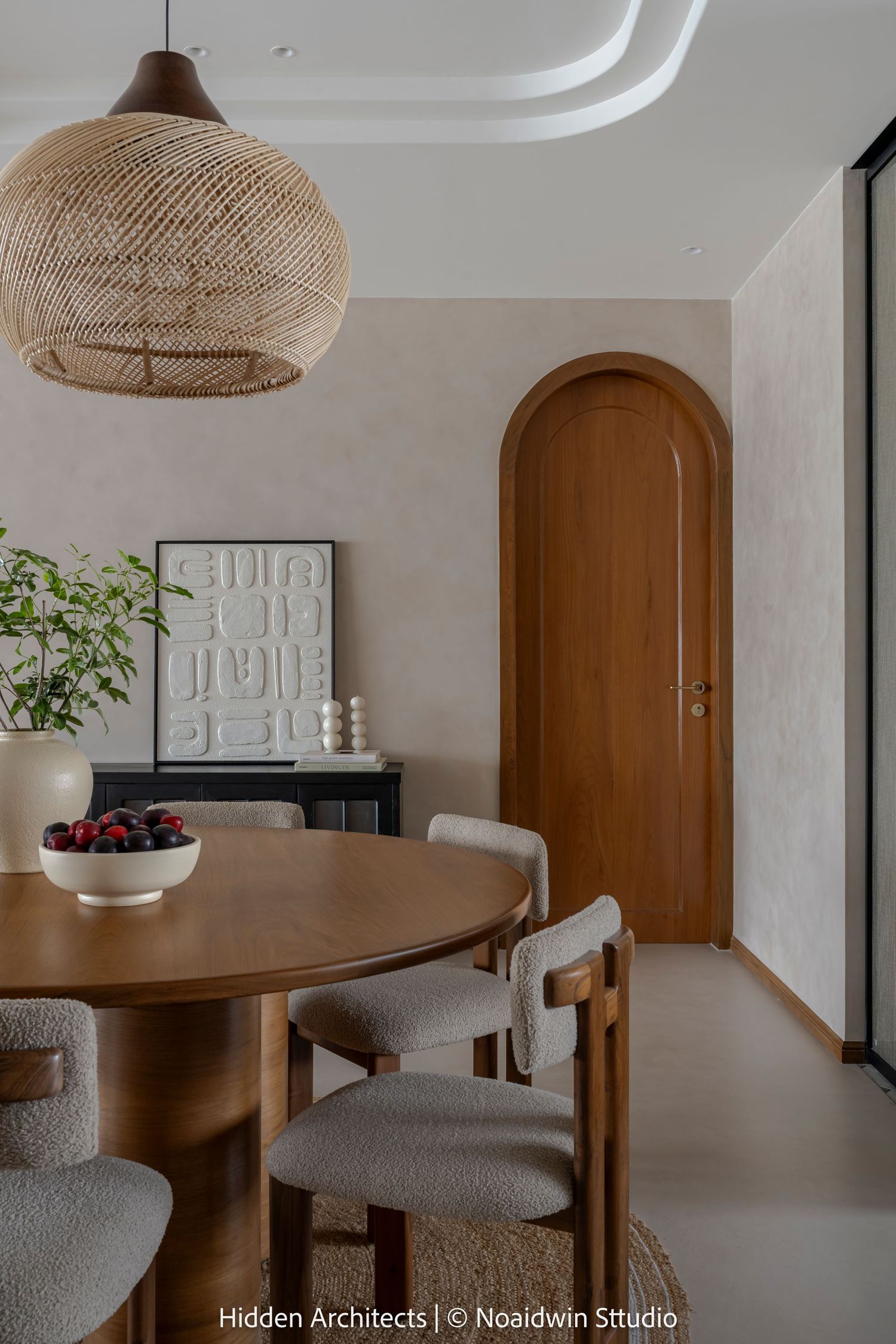 Warm dining room with round wooden table, boucle chairs, woven pendant light, and arched wooden door.
