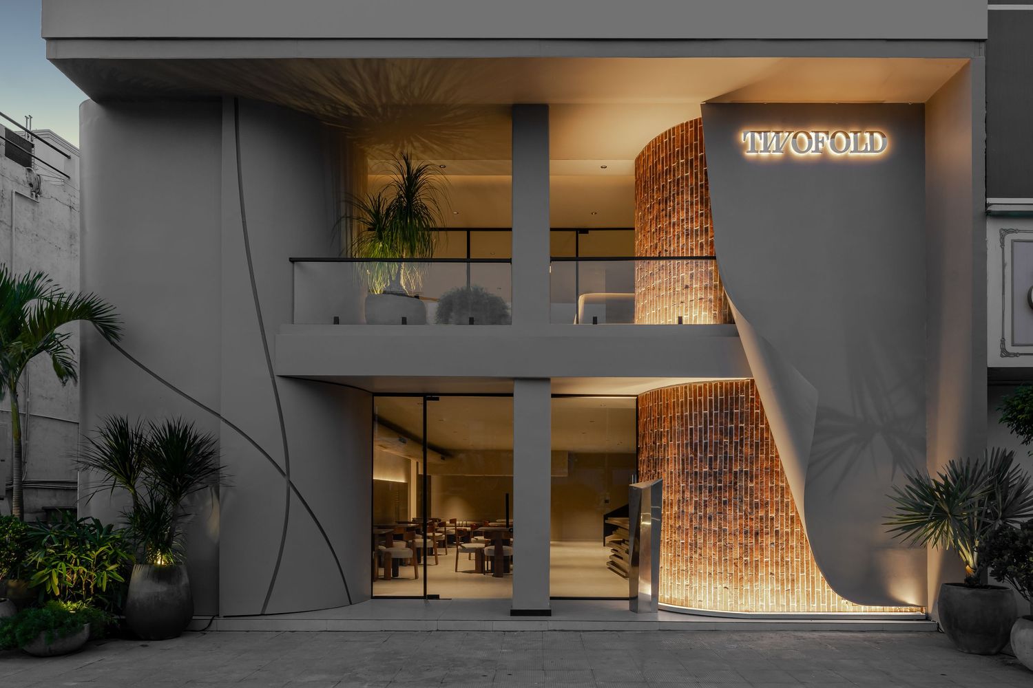 Contemporary restaurant entrance with illuminated signage, stone accent wall, and tropical plants.