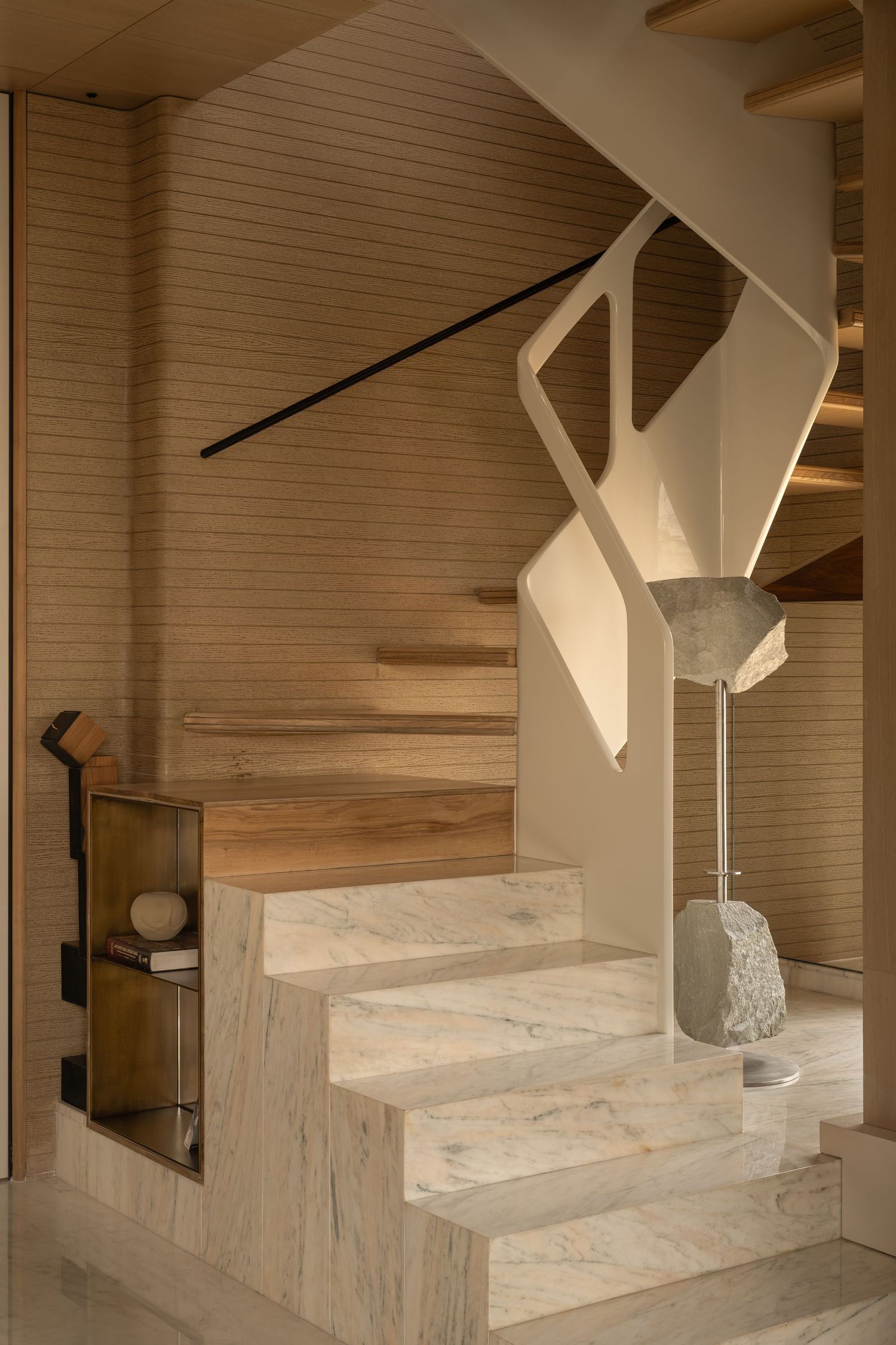 Elegant staircase with marble steps, wooden treads, sculptural white railing, and stone lamp.