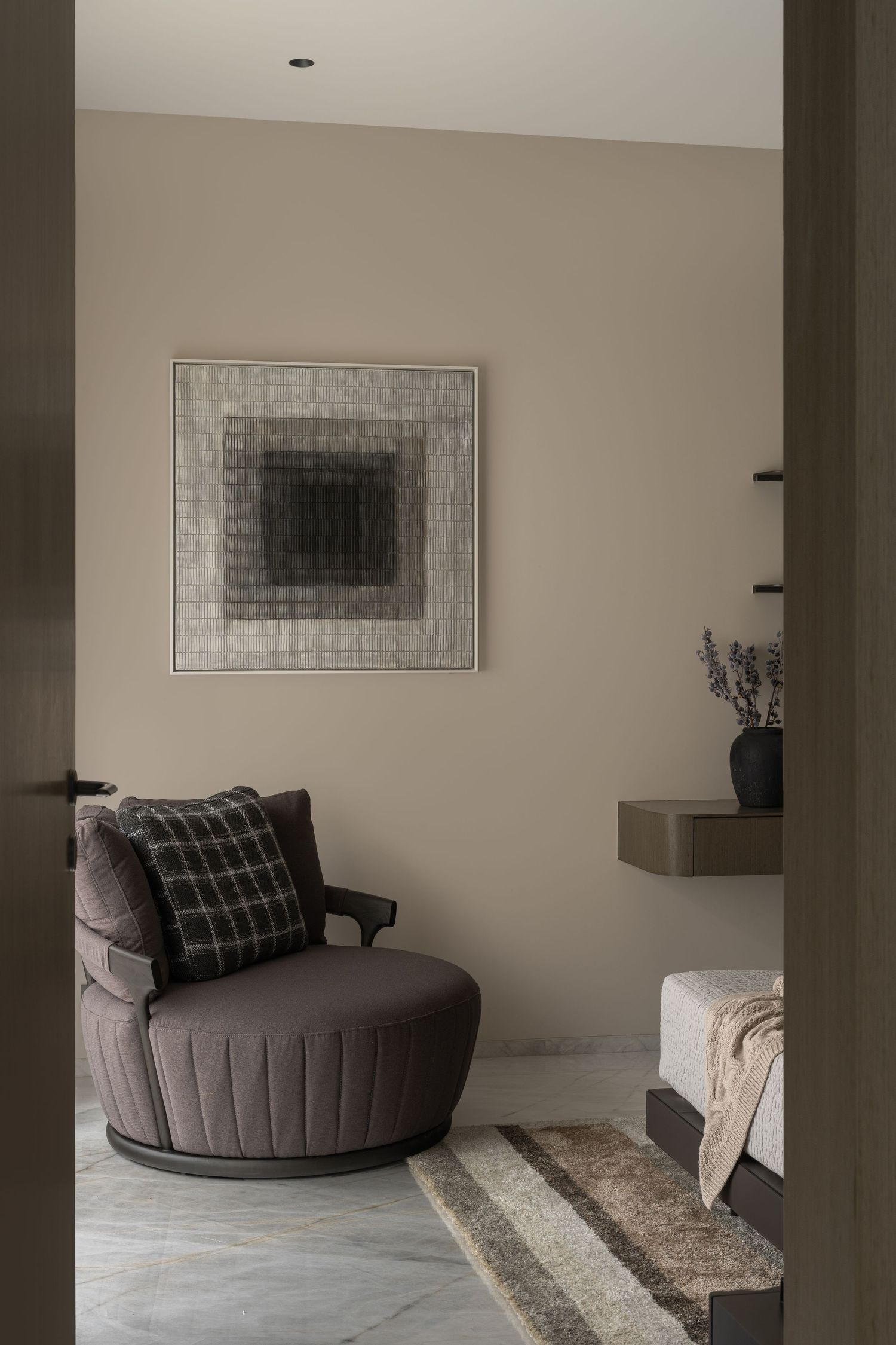 Cozy reading nook with round tufted swivel chair, geometric artwork, and floating shelf with lavender.
