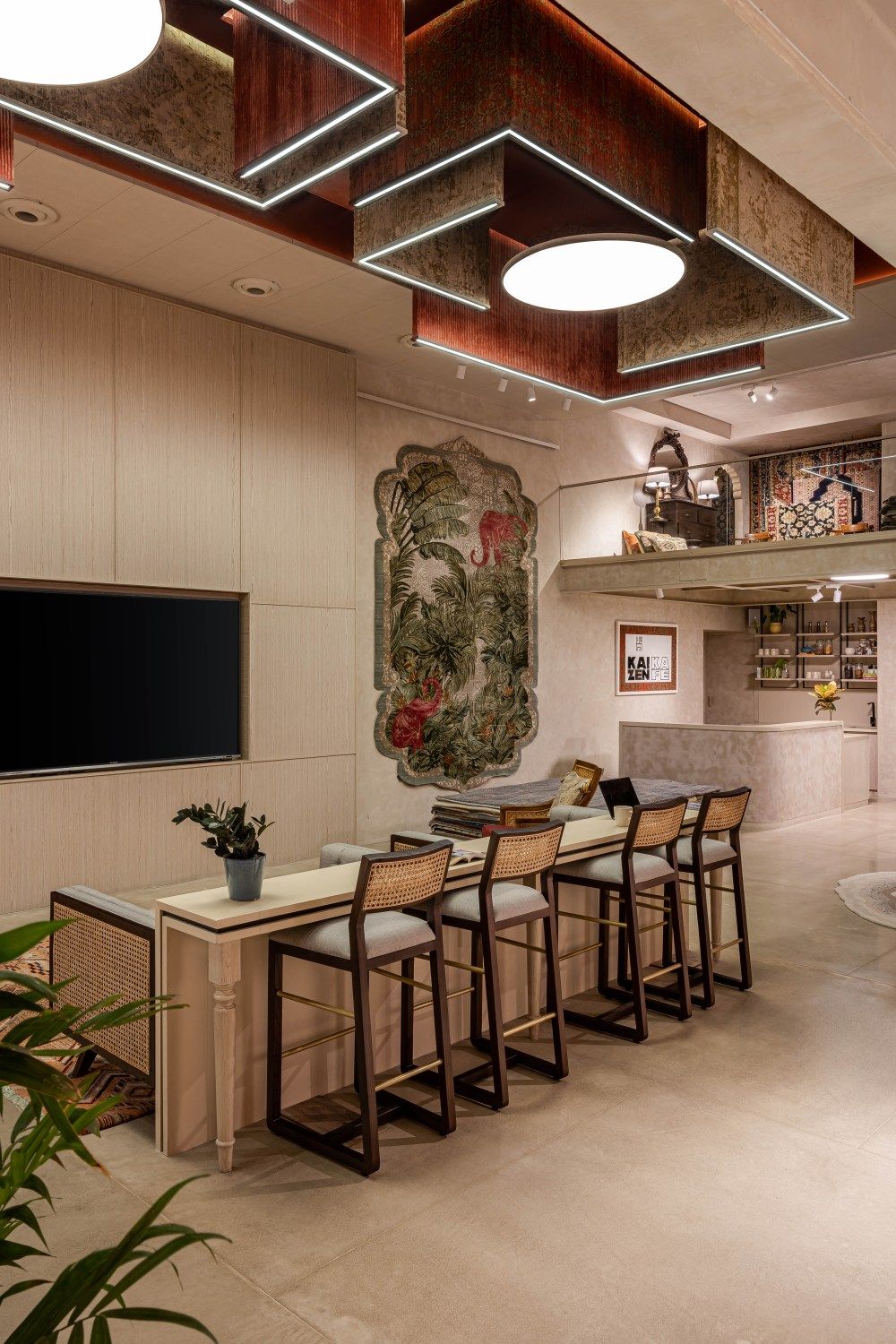 Stylish interior with bar stools, white counter, tropical mural wall art, TV panel, and decorative ceiling light fixtures.