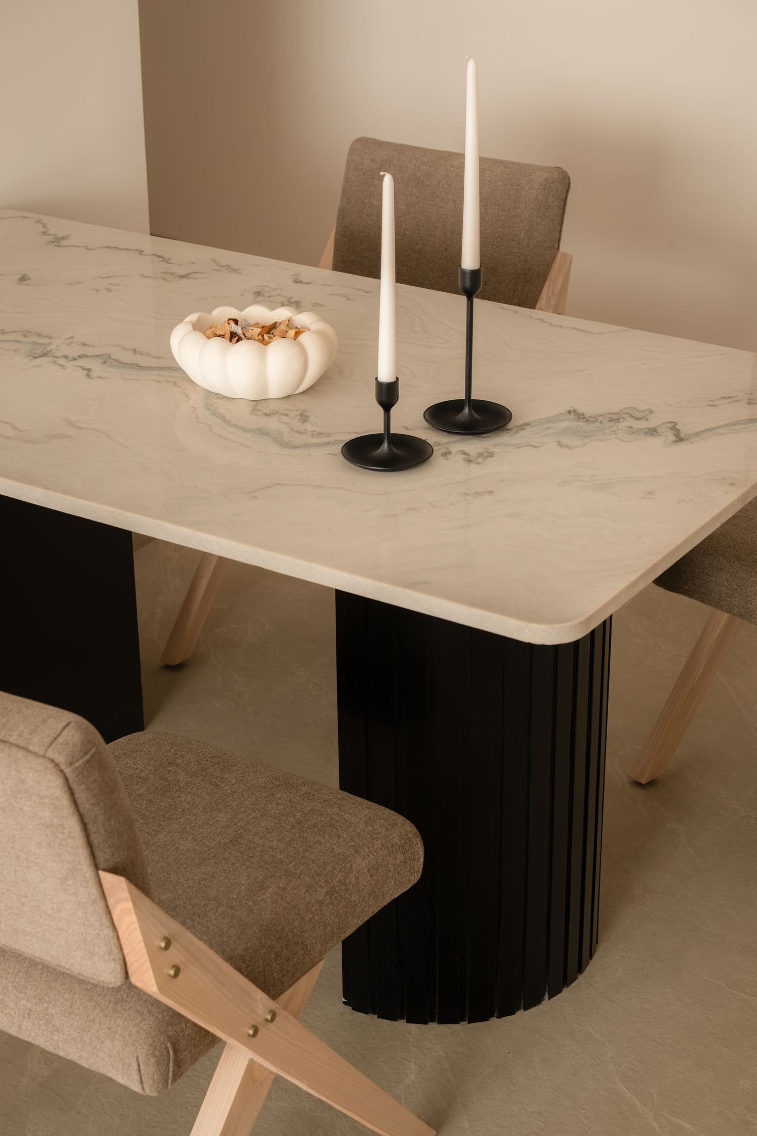 Elegant dining table with marble top, black fluted pedestal base, two candles, and beige upholstered chairs.