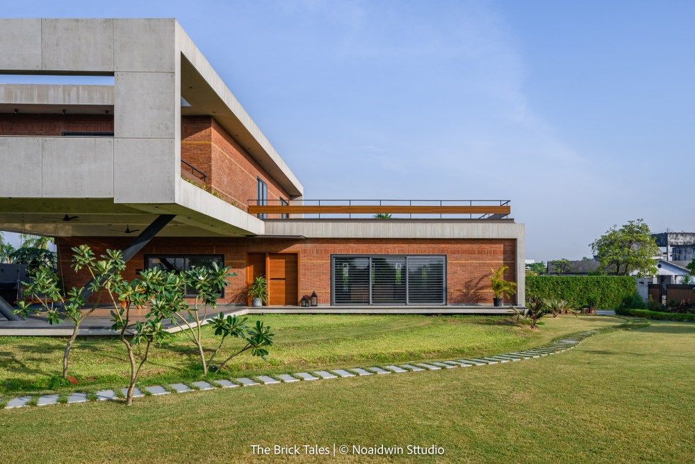 Side view of modern house with concrete upper story, red brick ground floor, large glass doors, and stepping stone path.