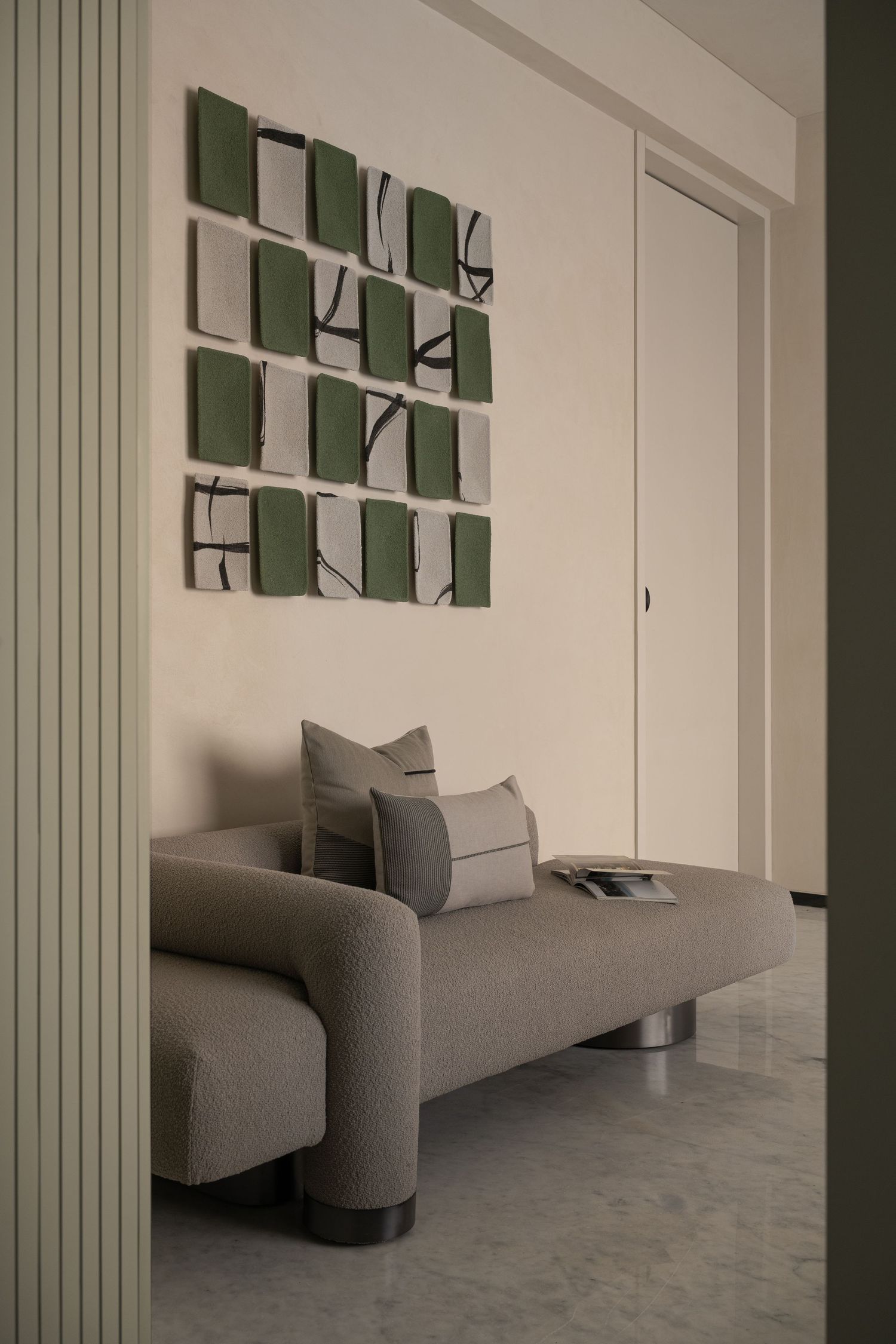 Minimalist entryway with gray curved bench, green abstract wall art panels, and marble floor.