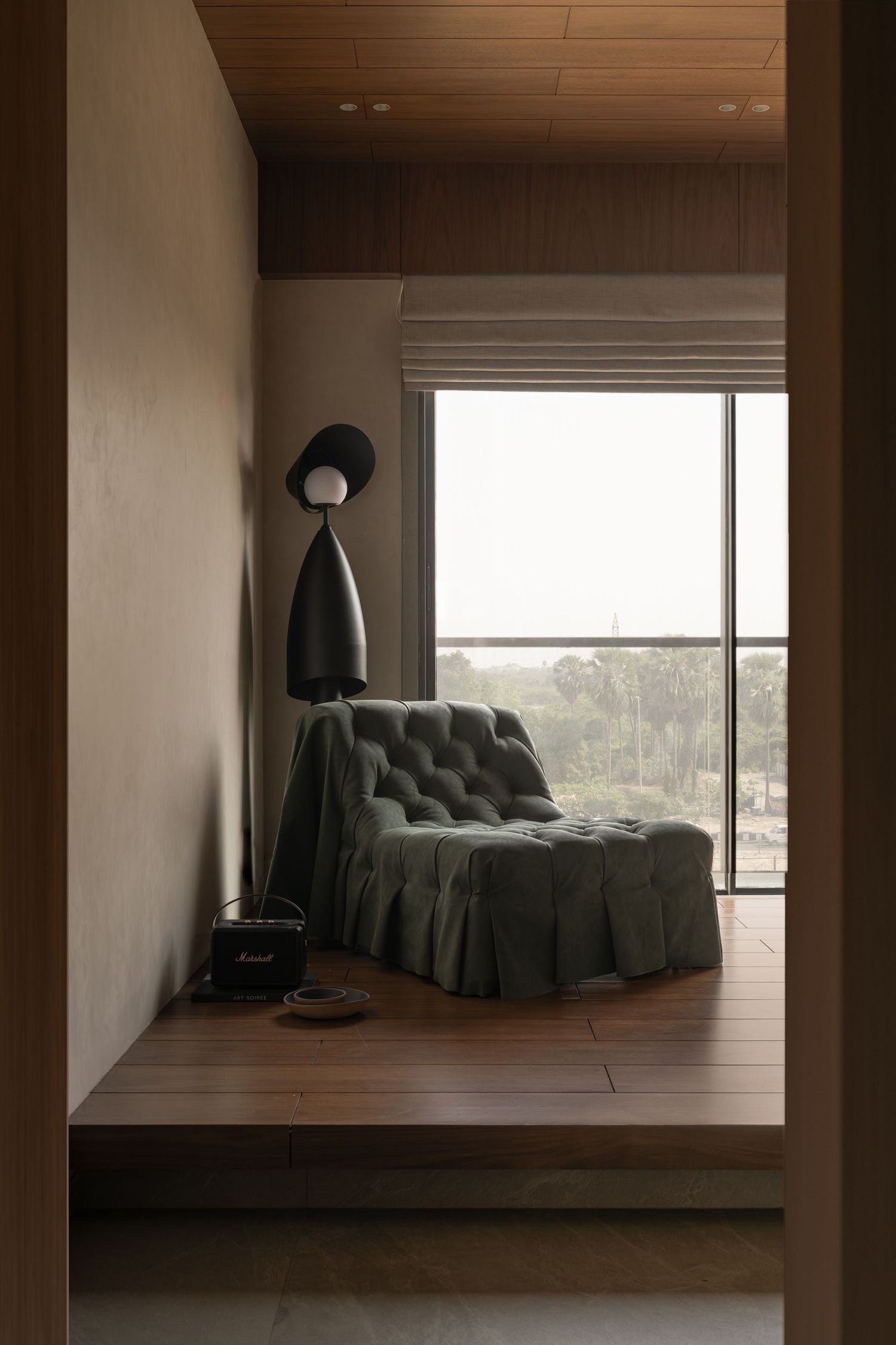 Cozy reading nook on raised wood platform with green tufted lounge chair, black floor lamp, and large window.