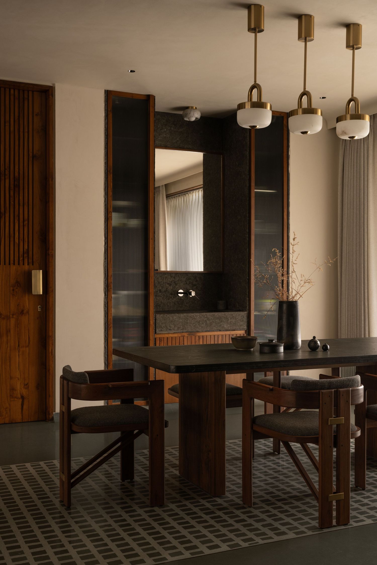 Sophisticated dining room with dark table, wooden chairs, brass pendant lights, and dark marble accent wall.