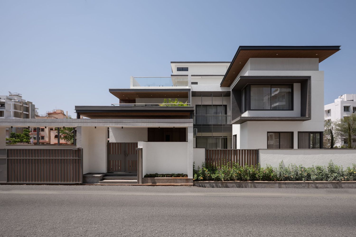 Modern two-story residential exterior with white and wood facade, flat roof overhangs, and decorative fence.