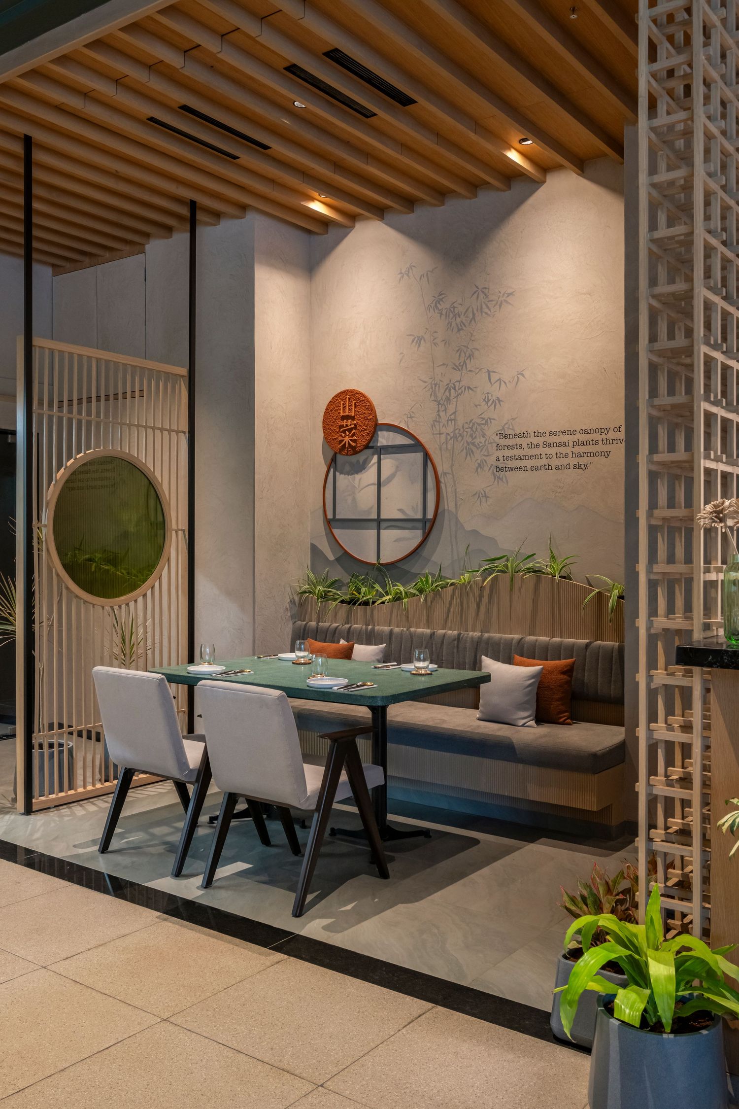 Intimate restaurant booth with concrete walls, green dining table, circular window detail, and wooden lattice divider.