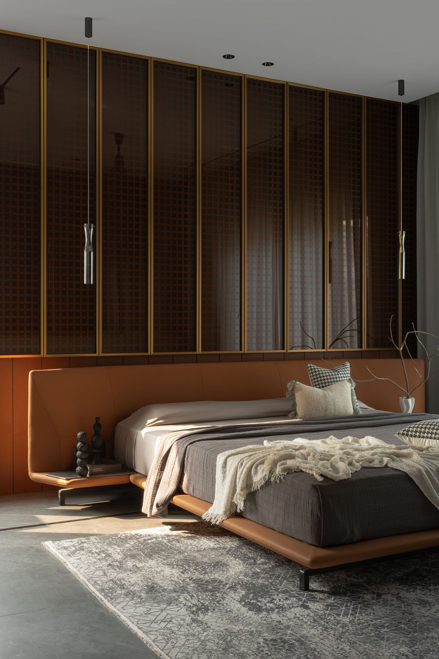 Luxurious modern bedroom with dark wood paneled wall, gold accents, orange leather bed frame, and pendant lights.