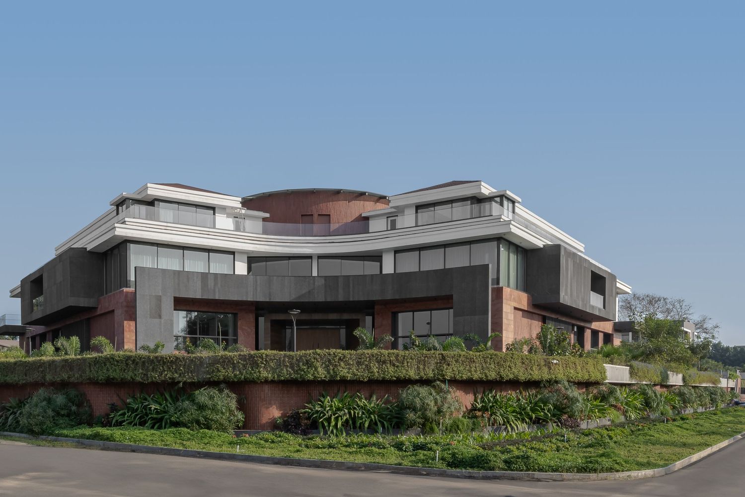 Modern curved commercial building with brick accents, glass facades, and green hedges.