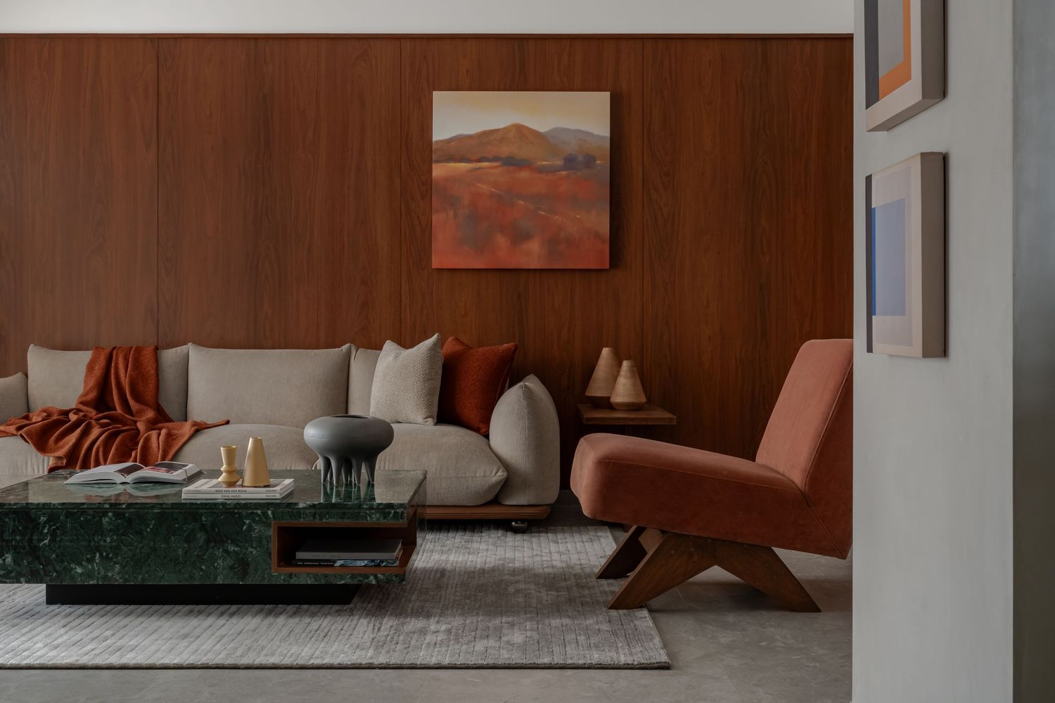 Warm living room with rich walnut wood paneling, neutral sofa, green marble coffee table, and terracotta accents.