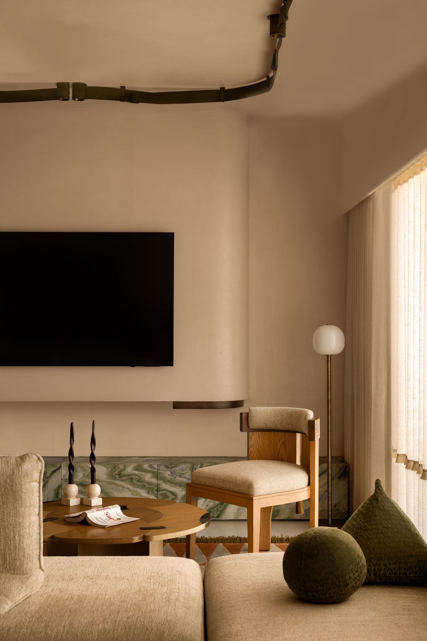 Cozy living room corner with wall-mounted TV, wooden chair, globe floor lamp, and green accents.