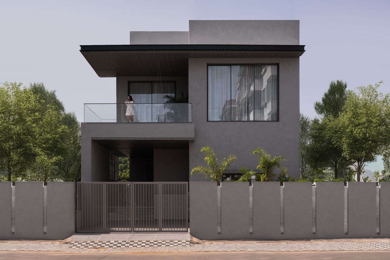 Sleek dark gray two-story modern home with cantilevered roof, glass balcony, and gated metal fence.
