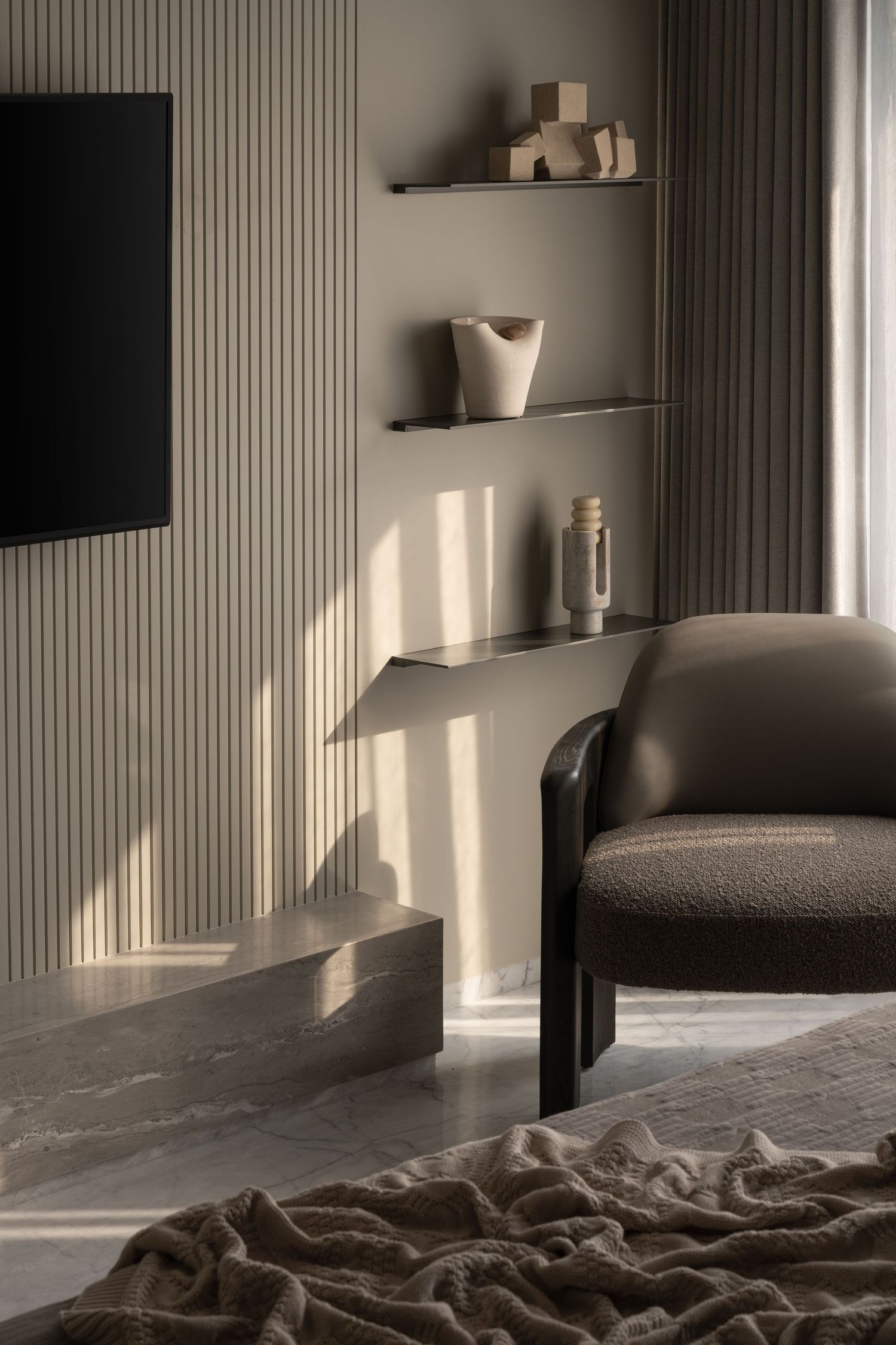 Modern bedroom corner with dark leather armchair, floating shelves, decorative objects, and marble floor.
