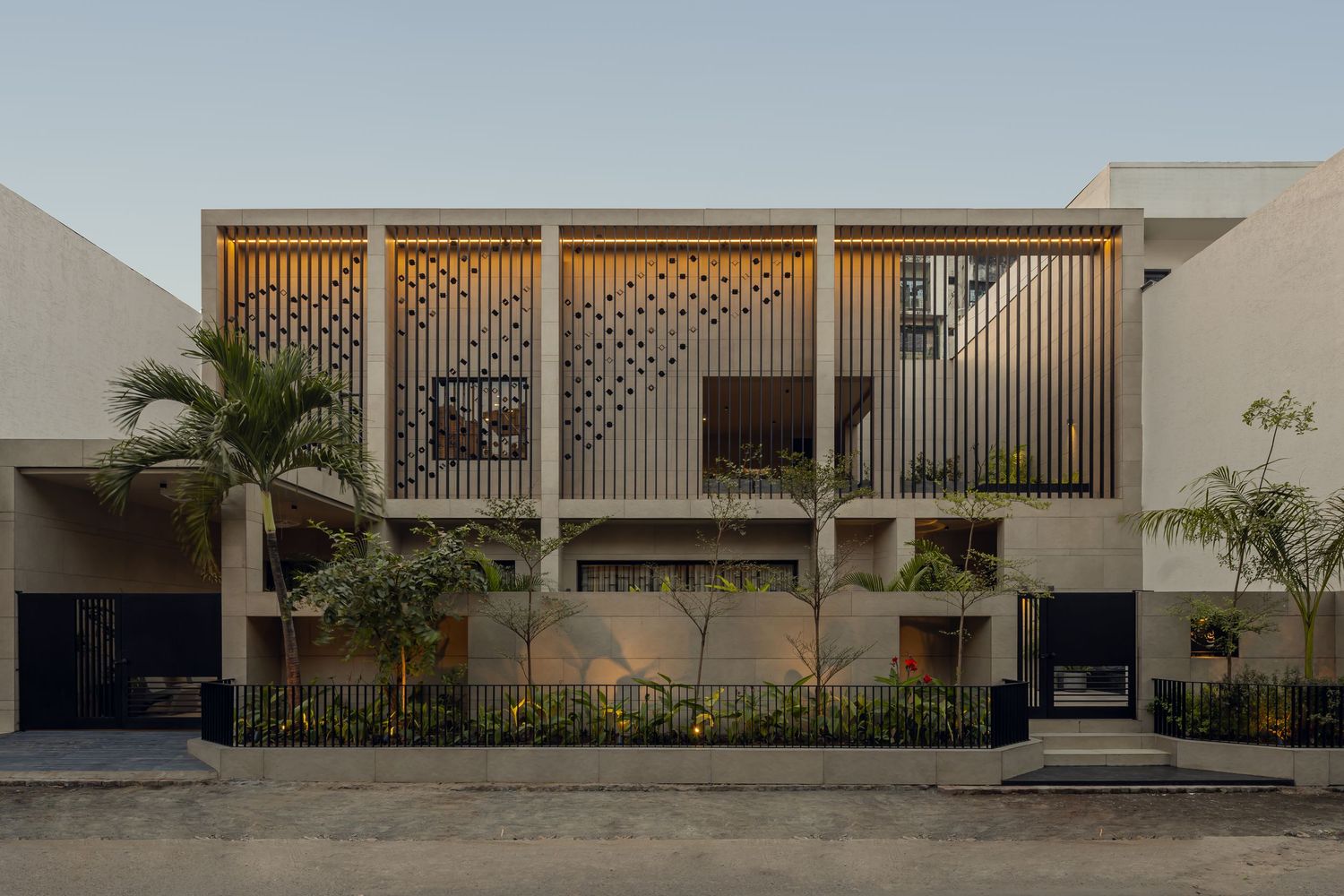 Contemporary two-story building facade with vertical louvers, decorative lattice screens, and lush tropical landscaping.
