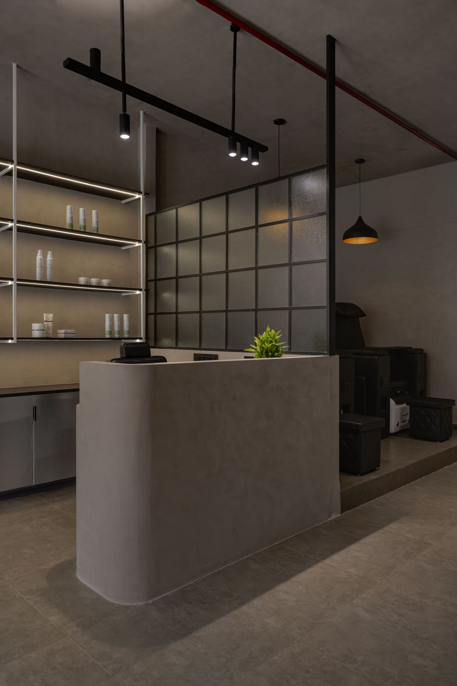 Modern salon reception desk in concrete finish with backlit shelving, grid partition wall, and pendant lighting in dark interior.