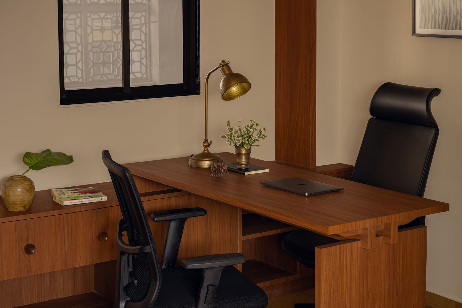 Compact home office with walnut desk, black ergonomic chair, brass lamp, and warm beige walls with subtle window light.