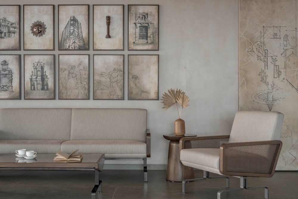 Refined living space with linen sofa, rattan armchair, architectural sketch gallery wall, and concrete floors.