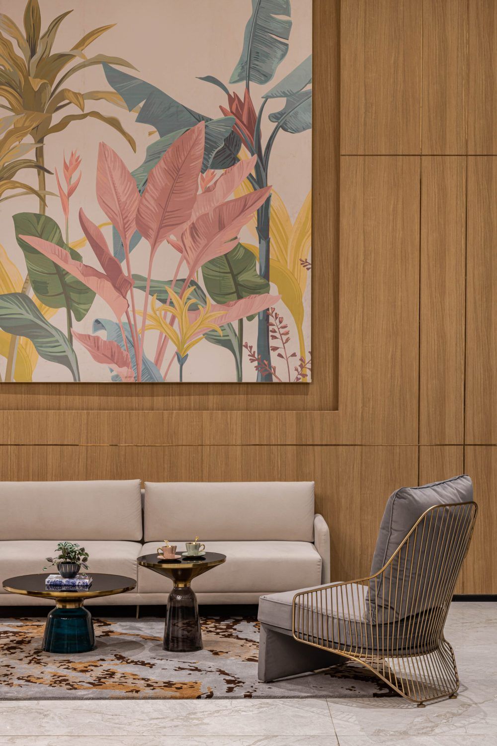 Warm hotel lobby seating area featuring tropical botanical mural, beige sofa, and gold-accented armchair on marble floor.