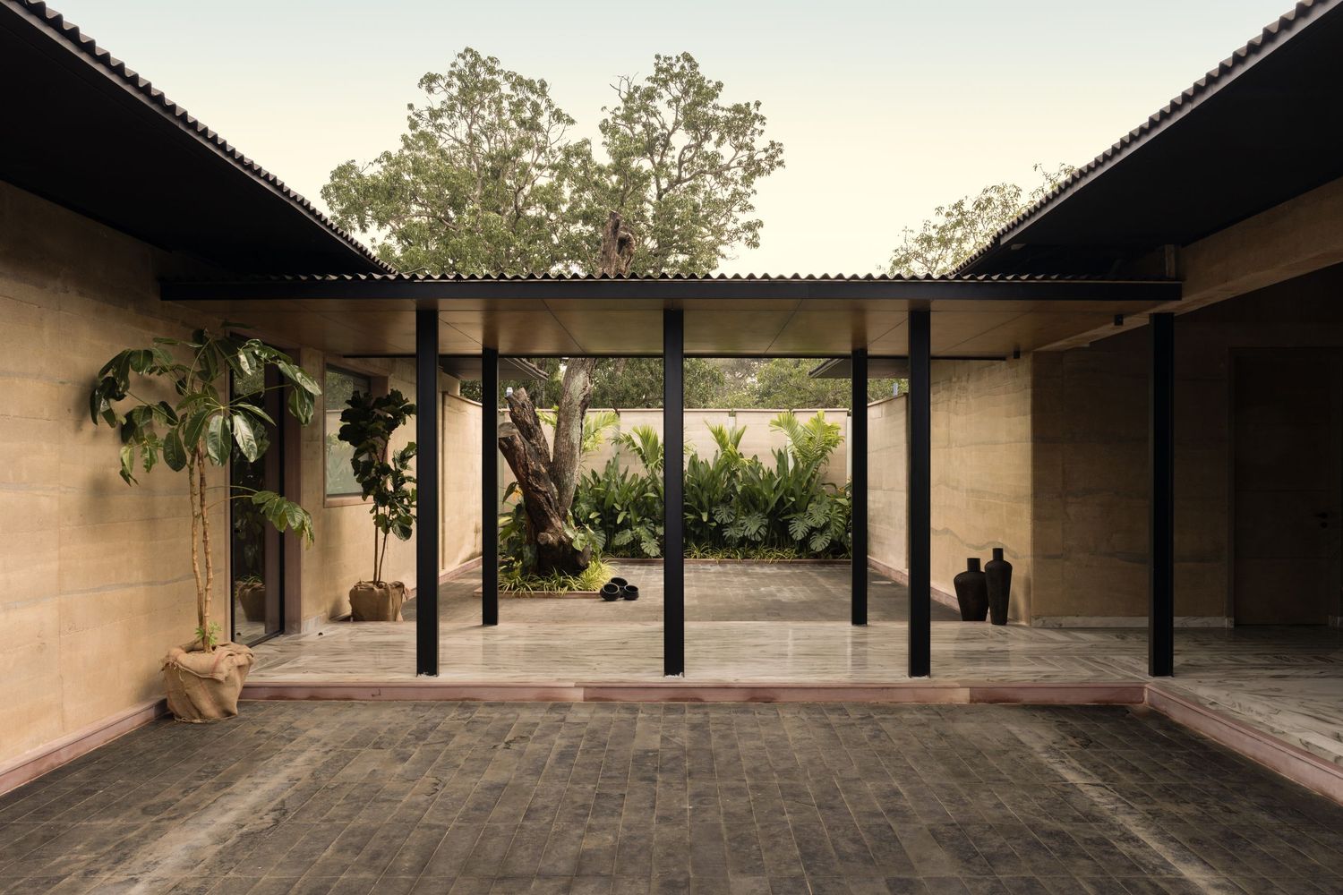 Open courtyard with black steel columns, stone walls, and tropical plants at dusk.