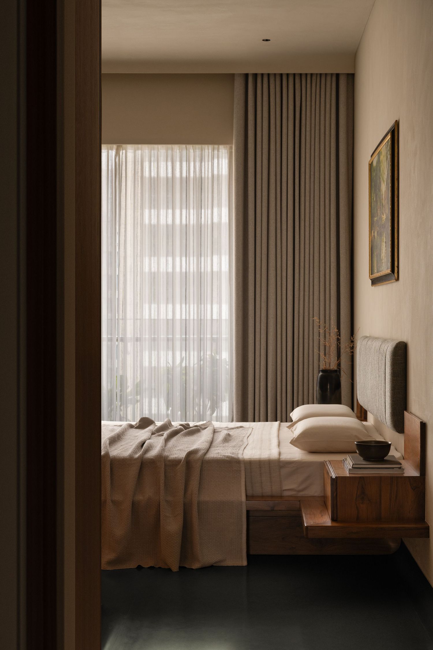 Serene bedroom with wooden bed frame, neutral linen bedding, sheer floor-to-ceiling curtains, and framed artwork.
