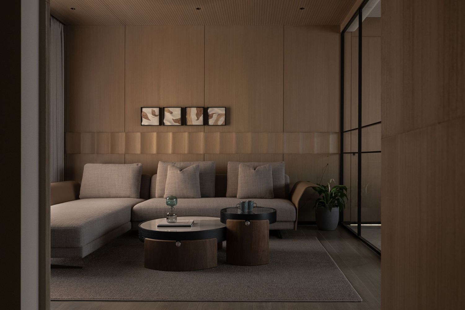 Elegant dimly lit living room featuring a beige tufted sofa, round wooden coffee tables, and warm wall panel lighting.