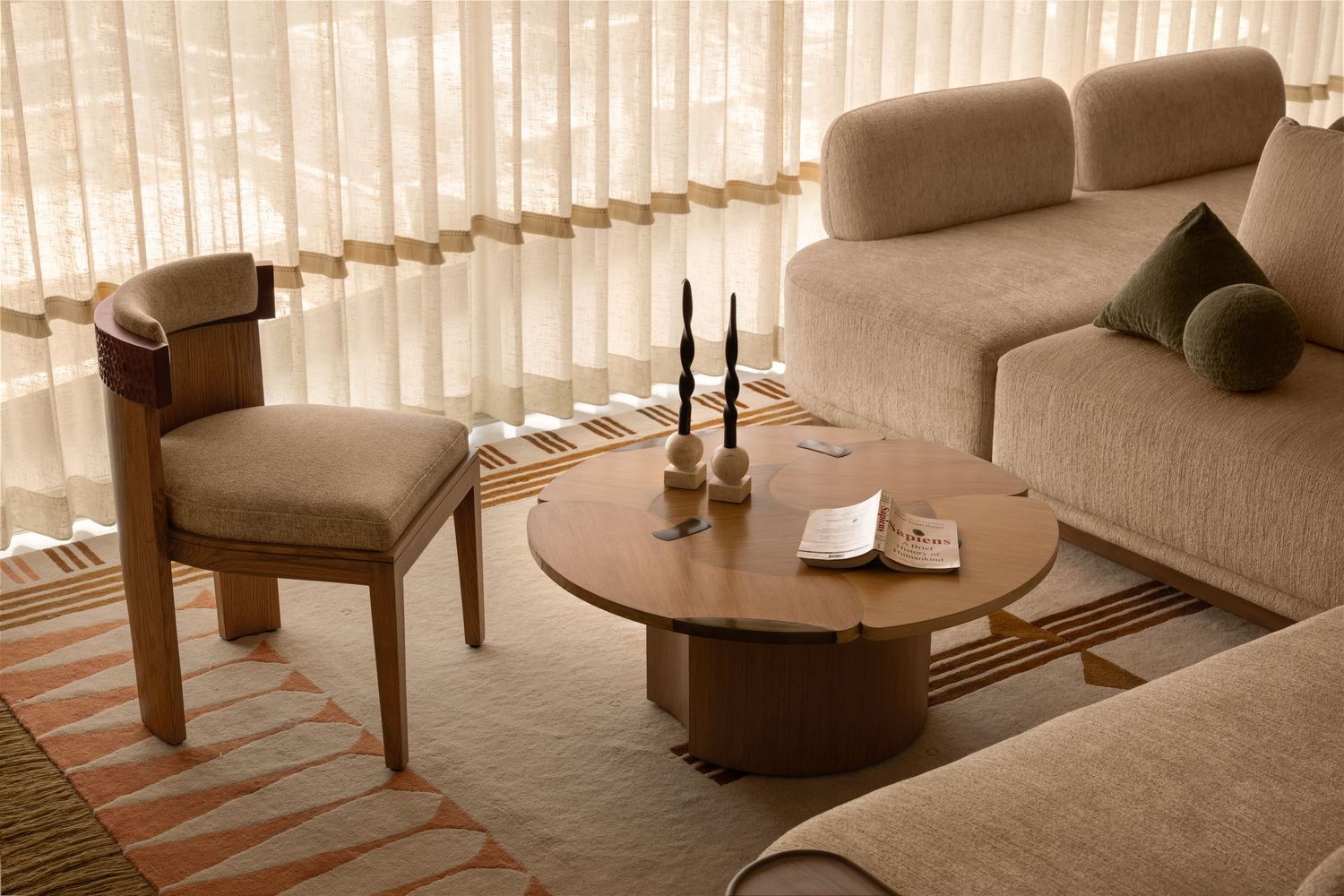Close-up of wooden armchair and round coffee table with candles on a patterned area rug.