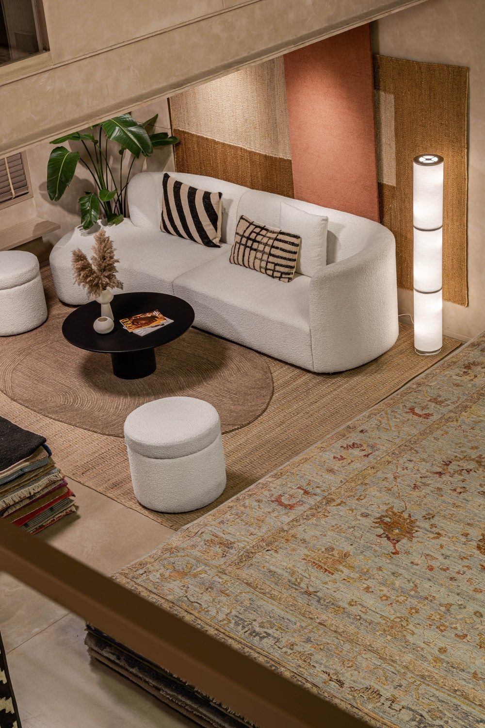 Cozy seating area with curved white sofa, black coffee table, white ottomans, floor lamp, and layered area rugs.