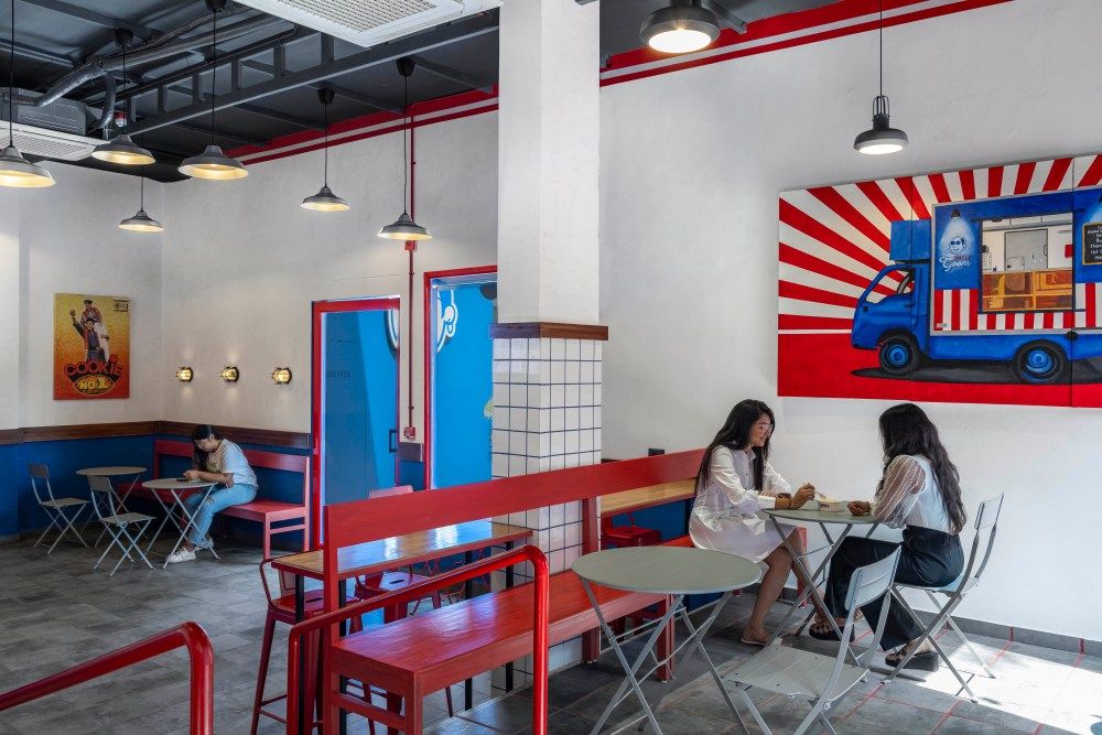 Trendy fast-casual restaurant with red and white decor, food truck mural, and customers dining at tables.
