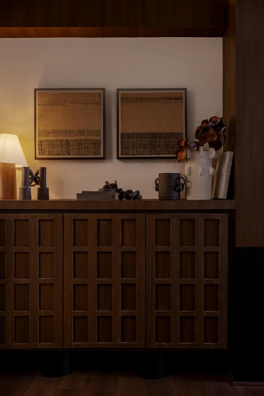 Dark wood sideboard with decorative vases, lamp, and framed abstract art in a warmly lit modern interior.