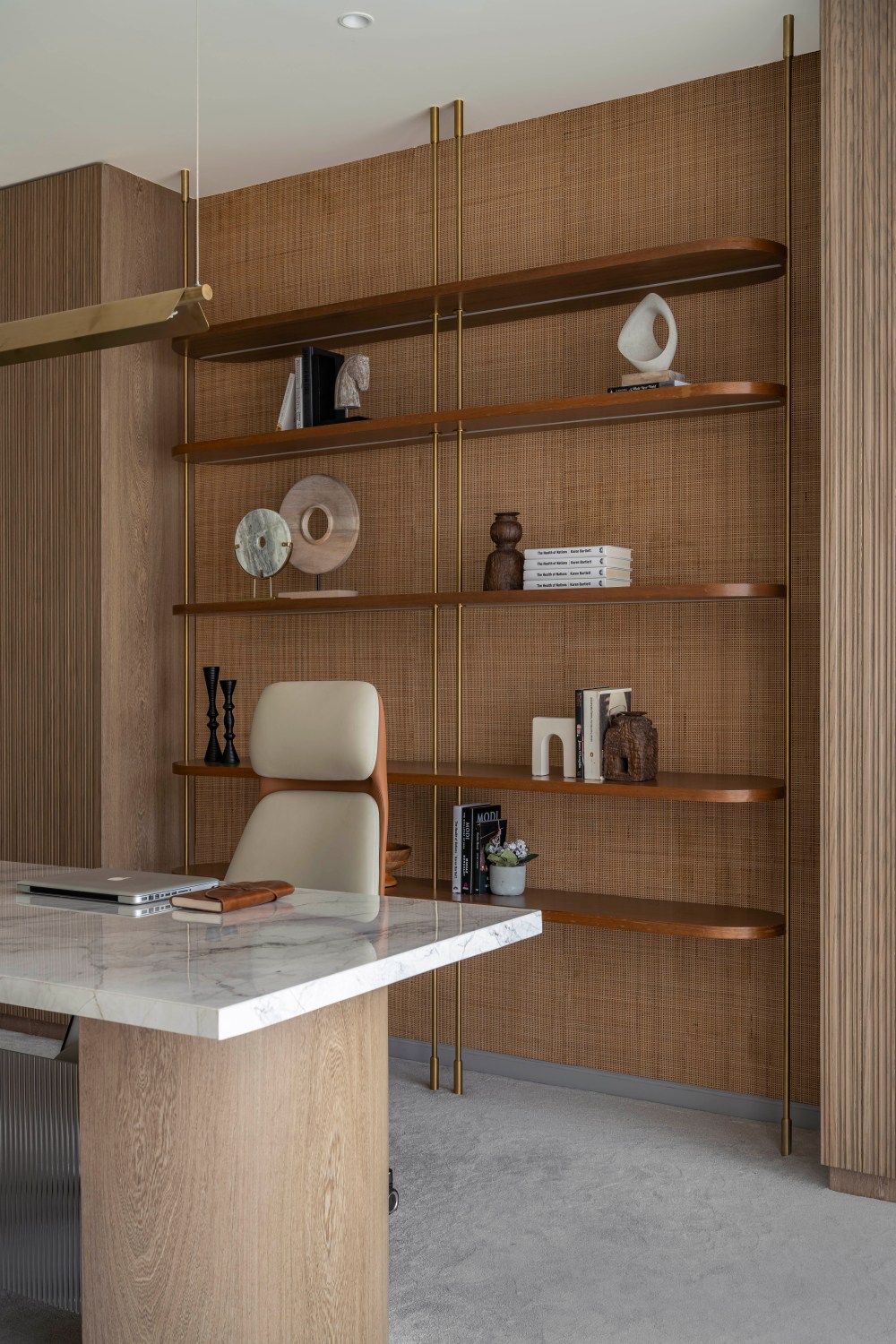 Upscale office with large wood shelving wall displaying decor, marble-top desk, and cream leather executive chair.
