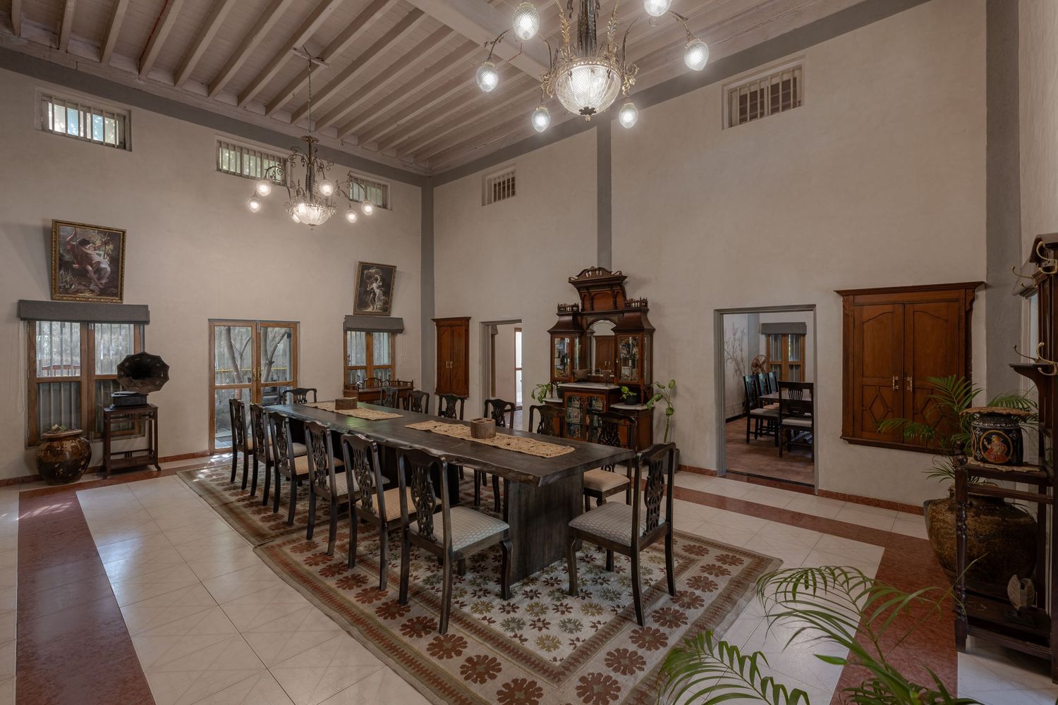 Grand colonial dining room with high beamed ceiling, long wooden table, chandelier, and ornate antique furnishings.