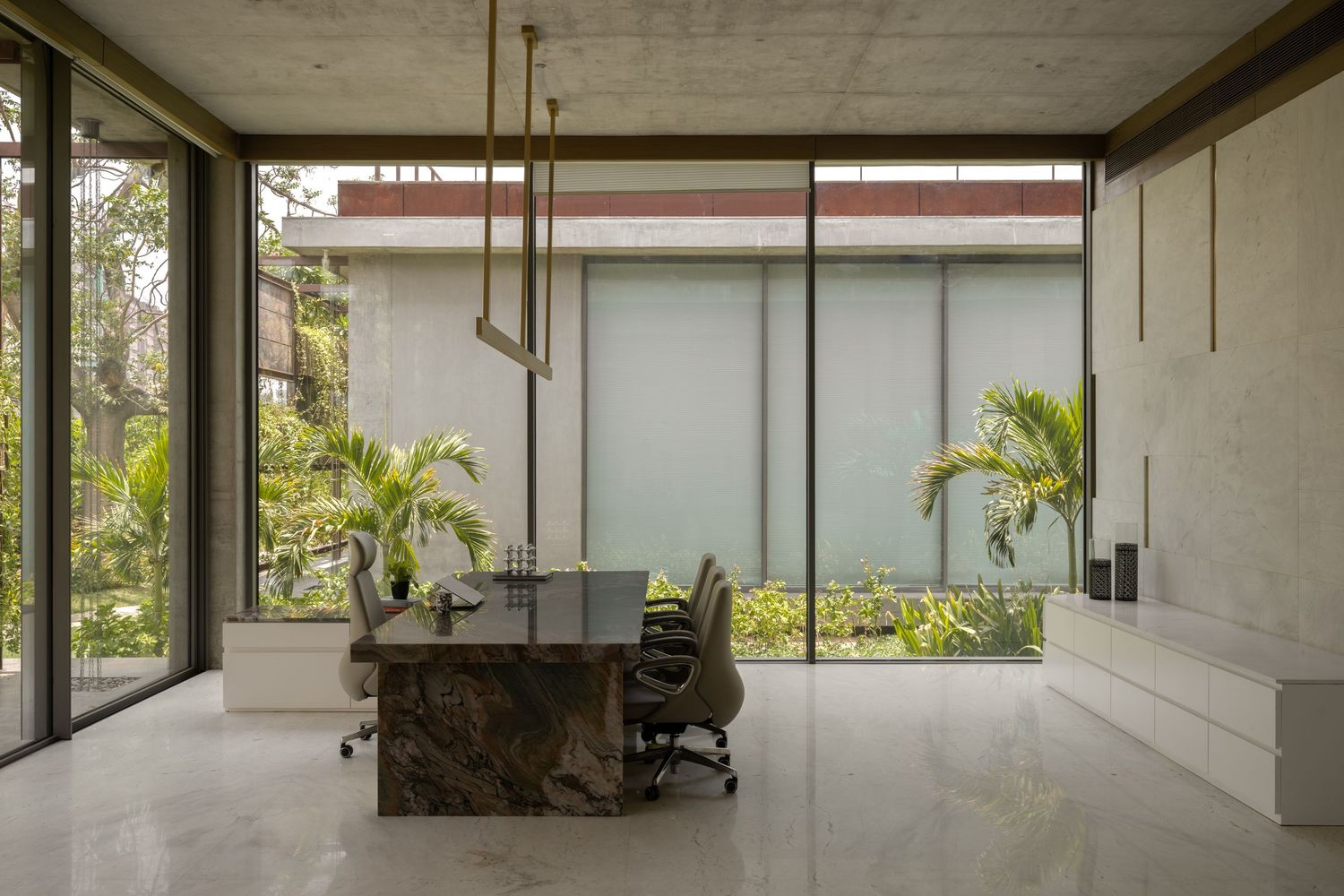 Modern office with marble desk, ergonomic chair, floor-to-ceiling windows, and lush tropical garden views in a minimalist space.