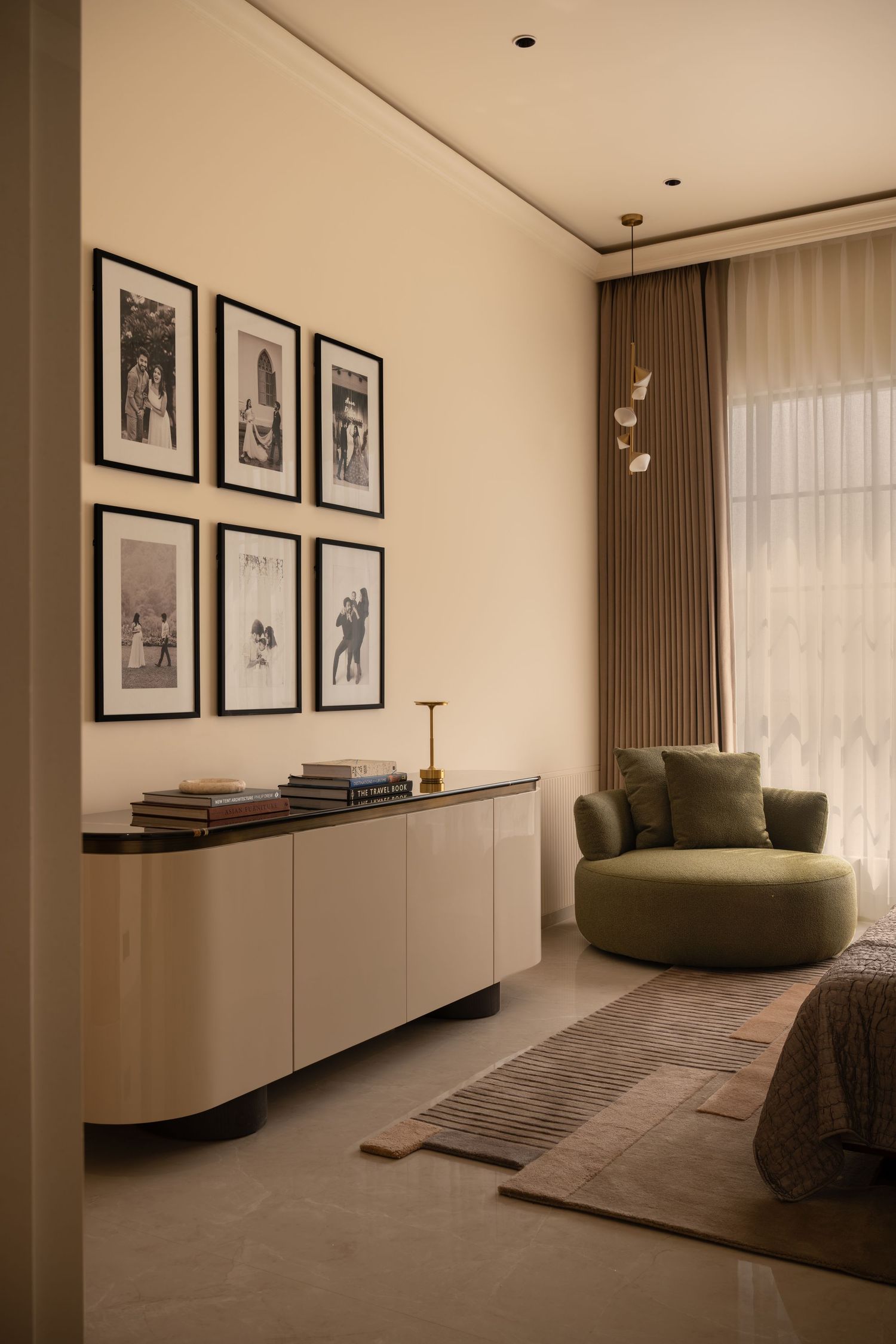 Modern bedroom sitting area with green accent chair, cream sideboard, and black-framed gallery wall.