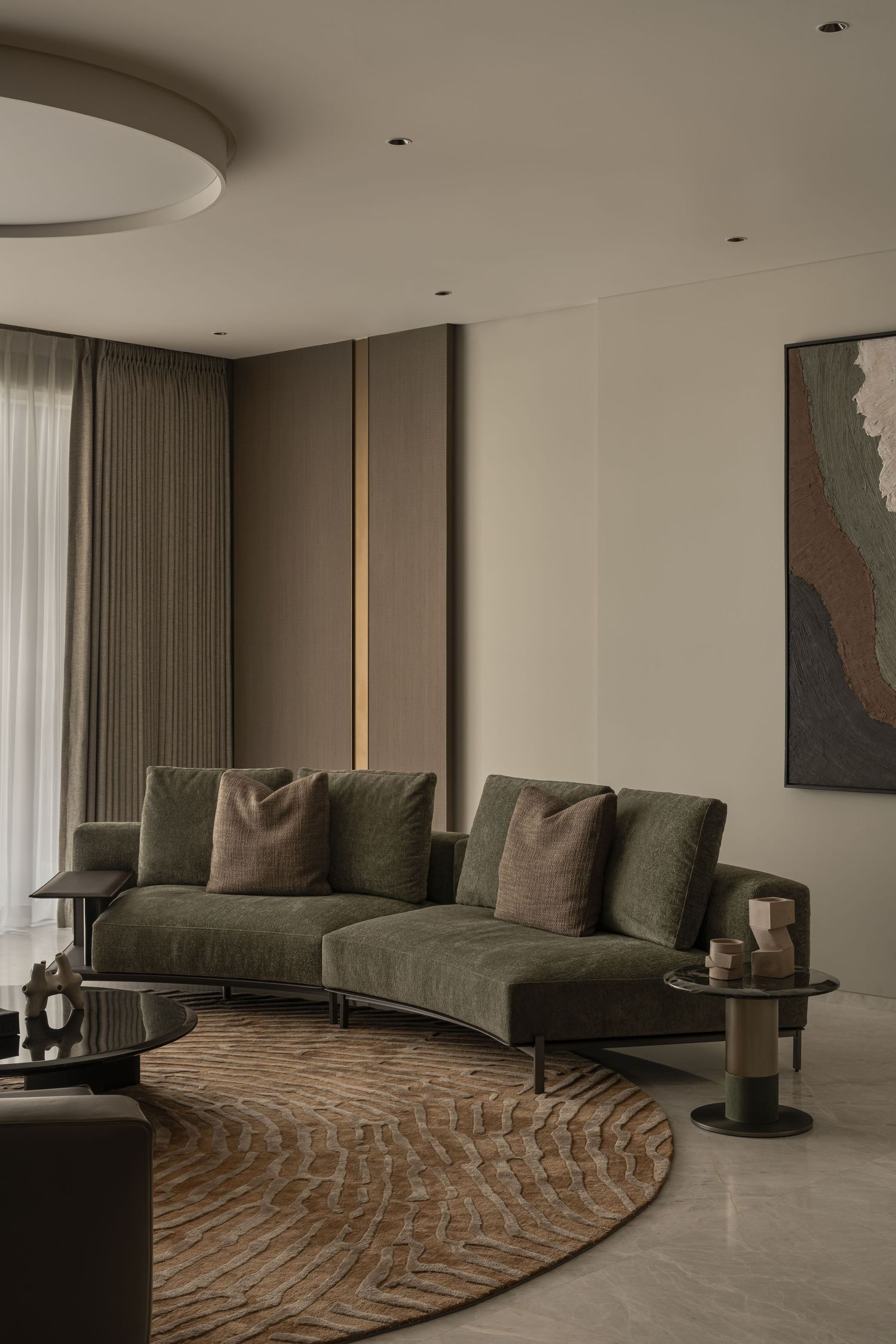 Modern living room with curved green sofa, circular rug, round ceiling light, and abstract wall art.