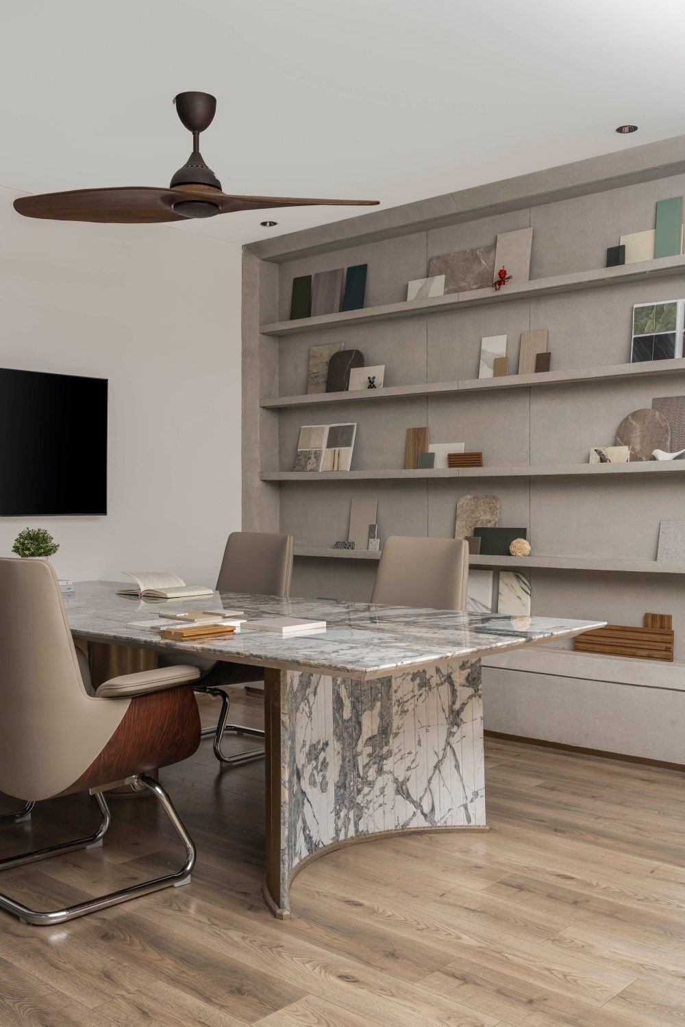 Stylish office interior with marble table, ceiling fan, built-in display shelves, and wall-mounted TV screen.