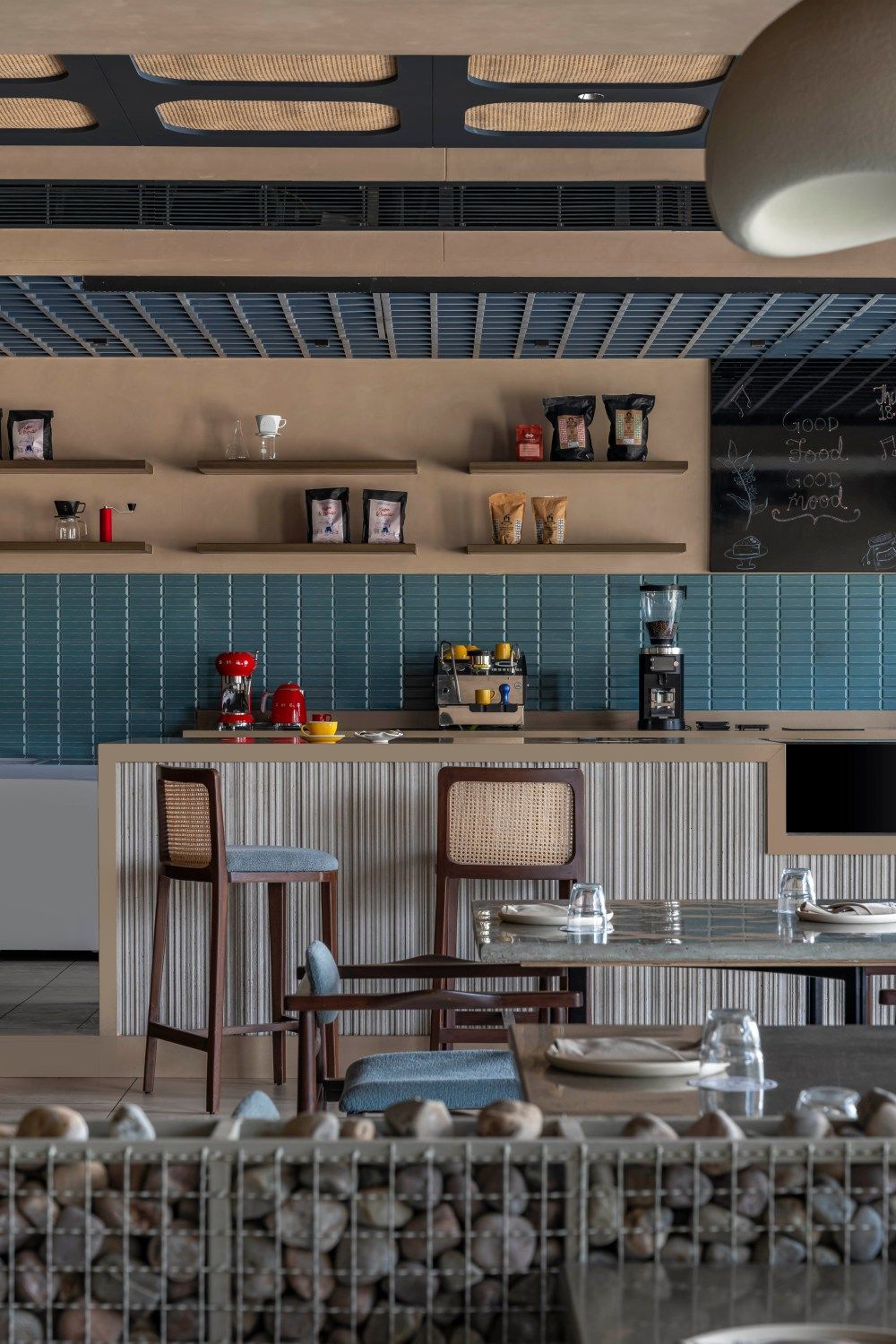 Restaurant coffee bar with blue subway tiles, open wooden shelves, striped counter, and rattan bar stools on display.