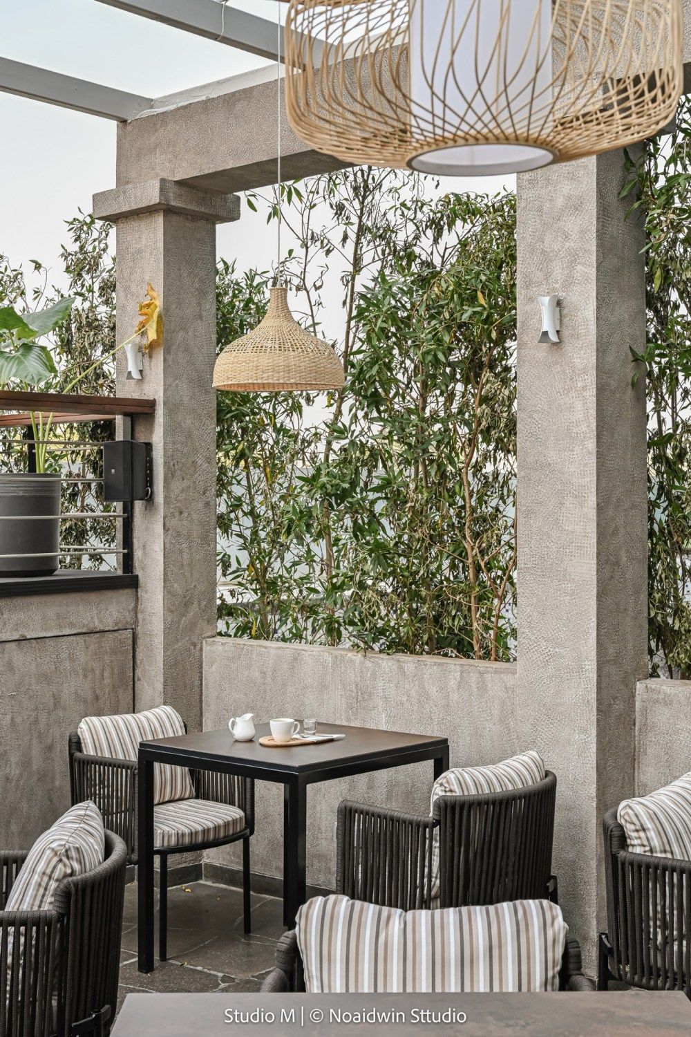 Outdoor patio dining area with striped cushioned chairs, wicker pendant light, and lush green plant wall.