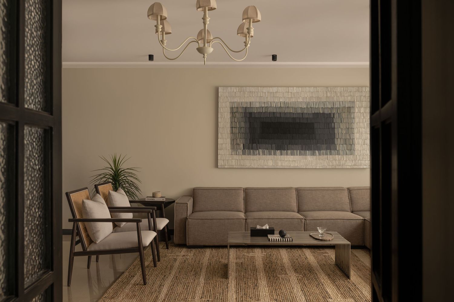 Contemporary living room with beige L-shaped sofa, abstract wall art, chandelier, and wood floor.