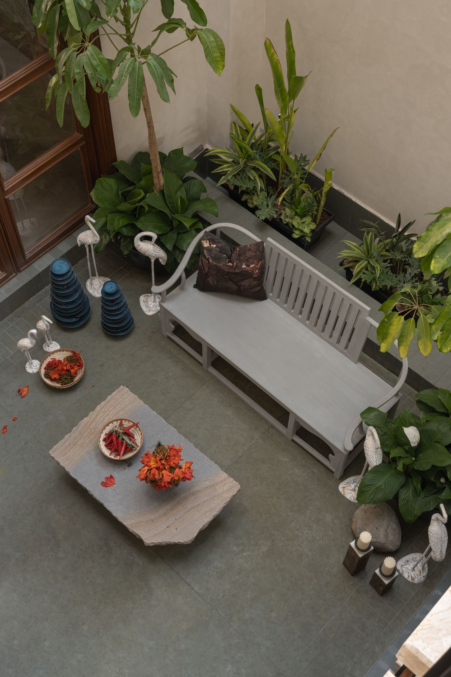 Aerial view of serene courtyard garden with grey bench, stone coffee table, and tropical plants.